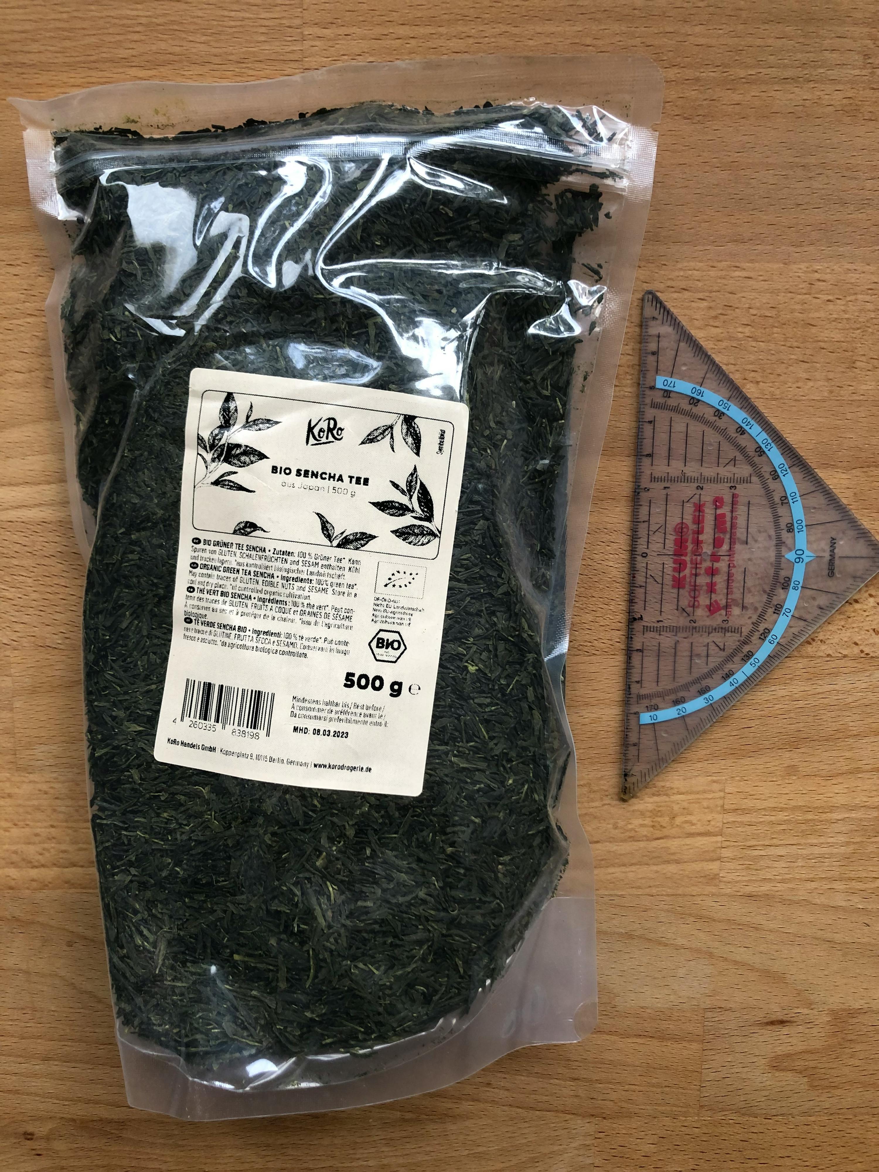 eine Tüte grüner Tee liegt auf einem Holztisch neben einem Dreieck