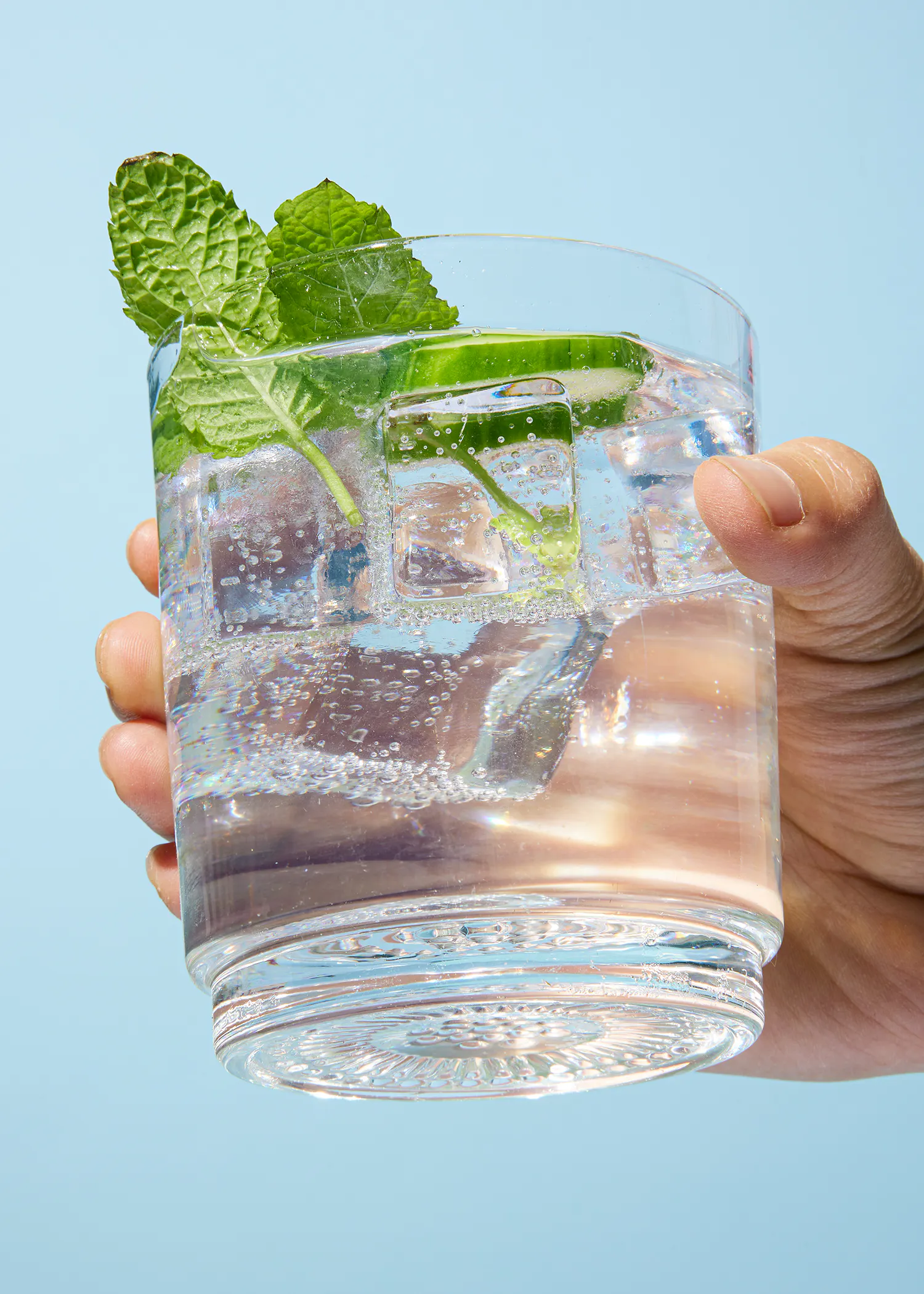 una persona sostiene un vaso de agua con cubitos de hielo y una rodaja de limón