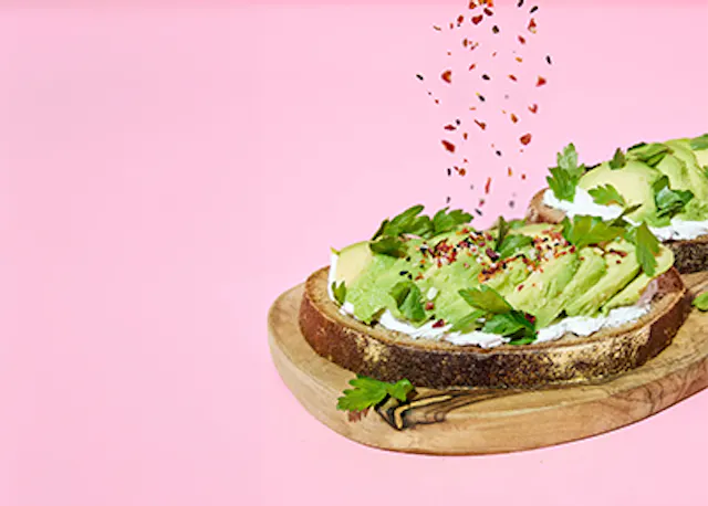 ein Stück Brot mit Avocado und Käse auf einem Schneidebrett .