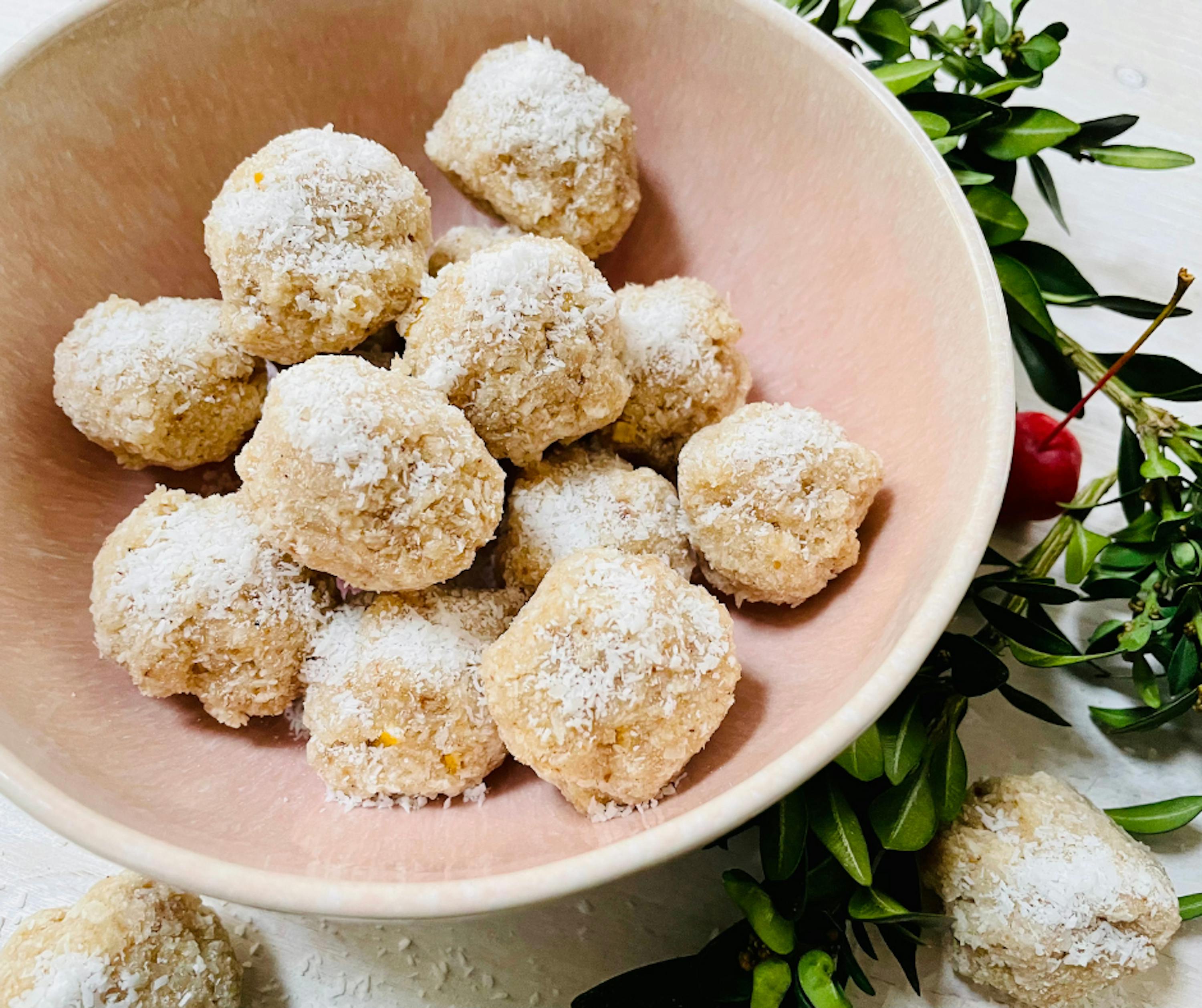 a pink bowl filled with coconut balls with powdered sugar on top