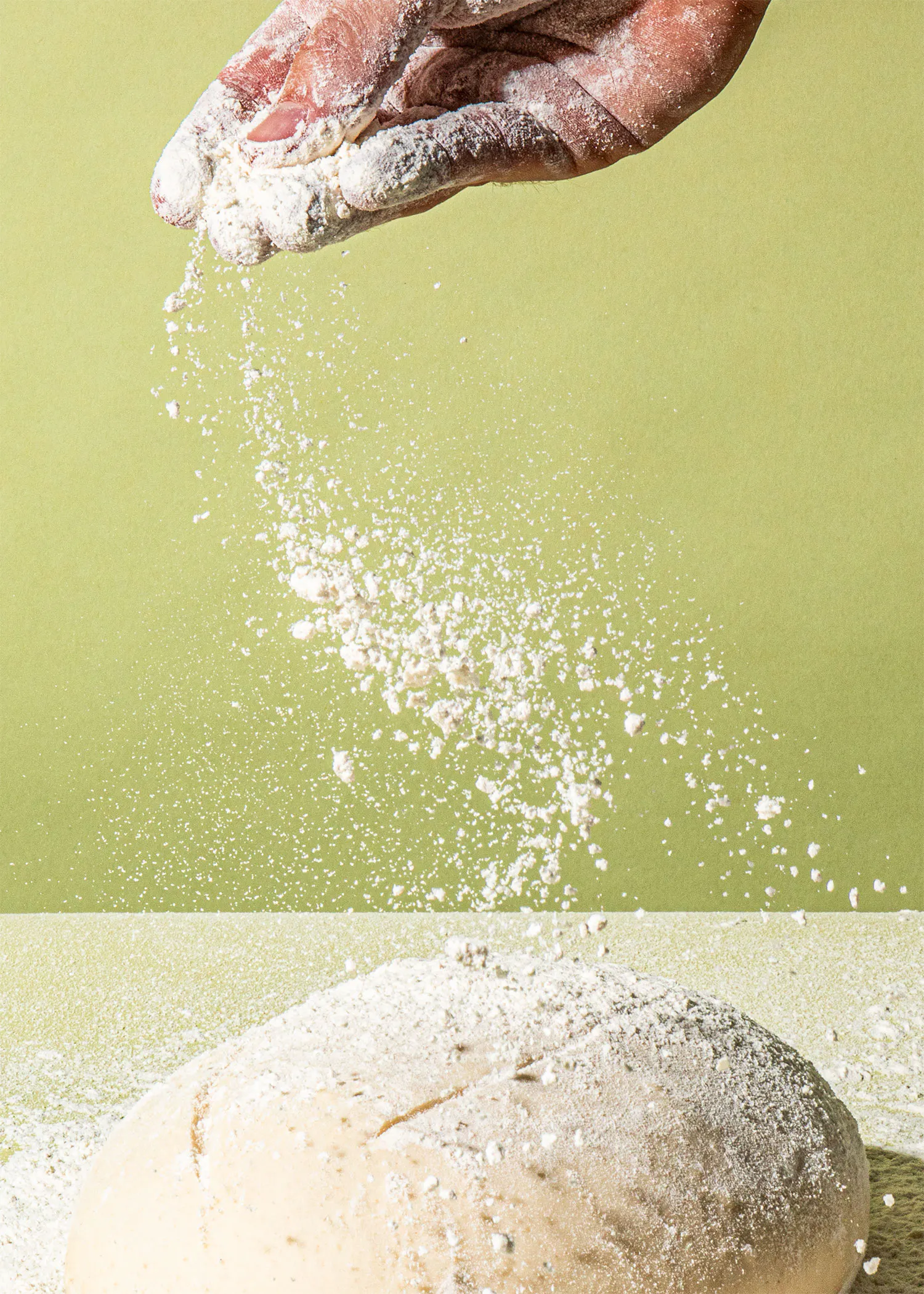 une personne jette de la farine sur un bol de pâte