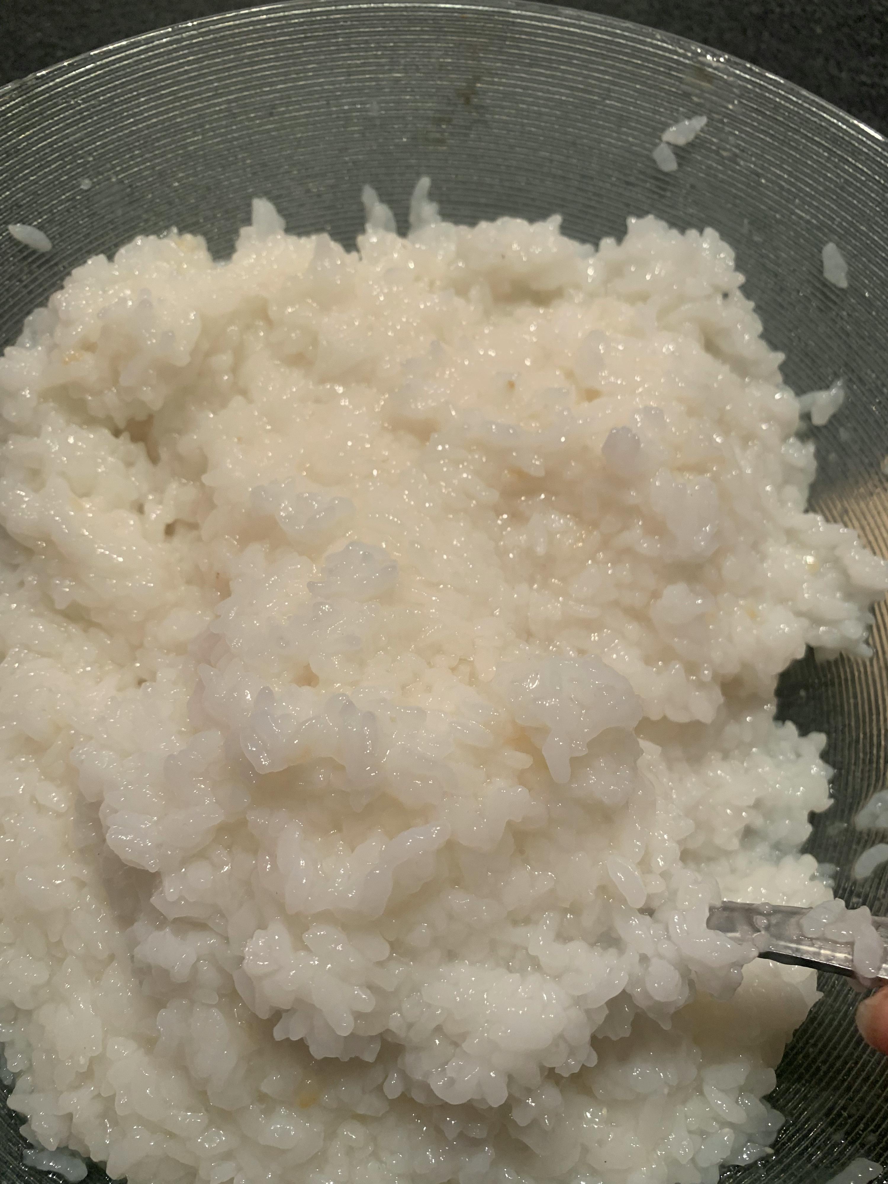a bowl of white rice is being stirred with a pair of tweezers