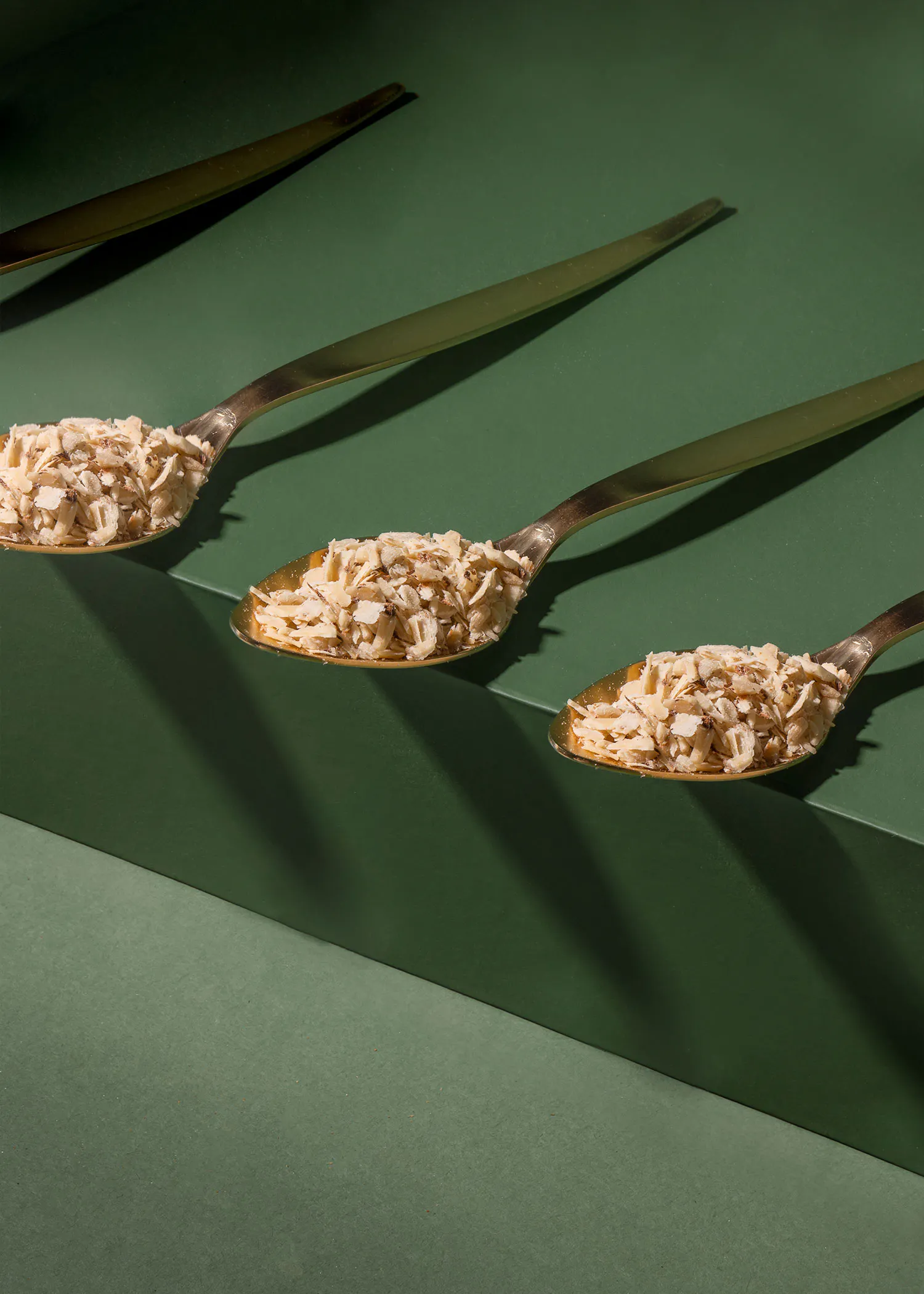trois cuillères remplies d' avoine sont alignées sur une surface verte