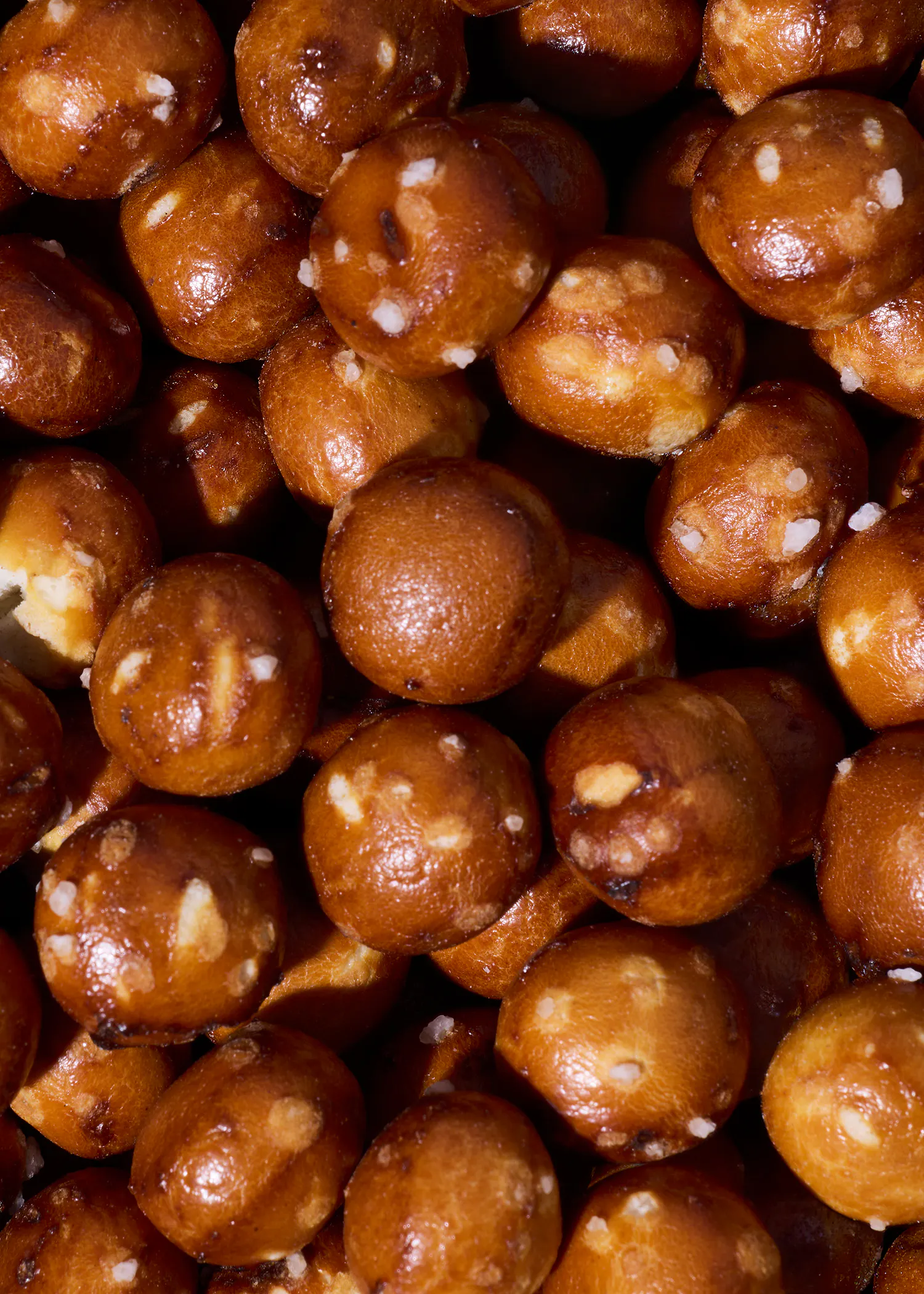 nahaufnahme von vielen kleinen, runden und goldbraun gebackenen laugenkonfekt-stücken, die mit grobem salz bestreut sind.
