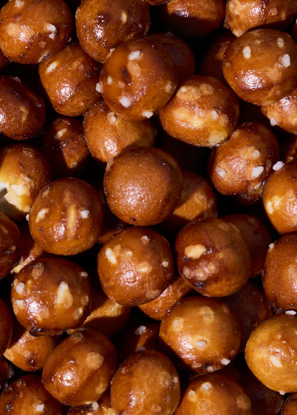 nahaufnahme von vielen kleinen, runden und goldbraun gebackenen laugenkonfekt-stücken, die mit grobem salz bestreut sind.