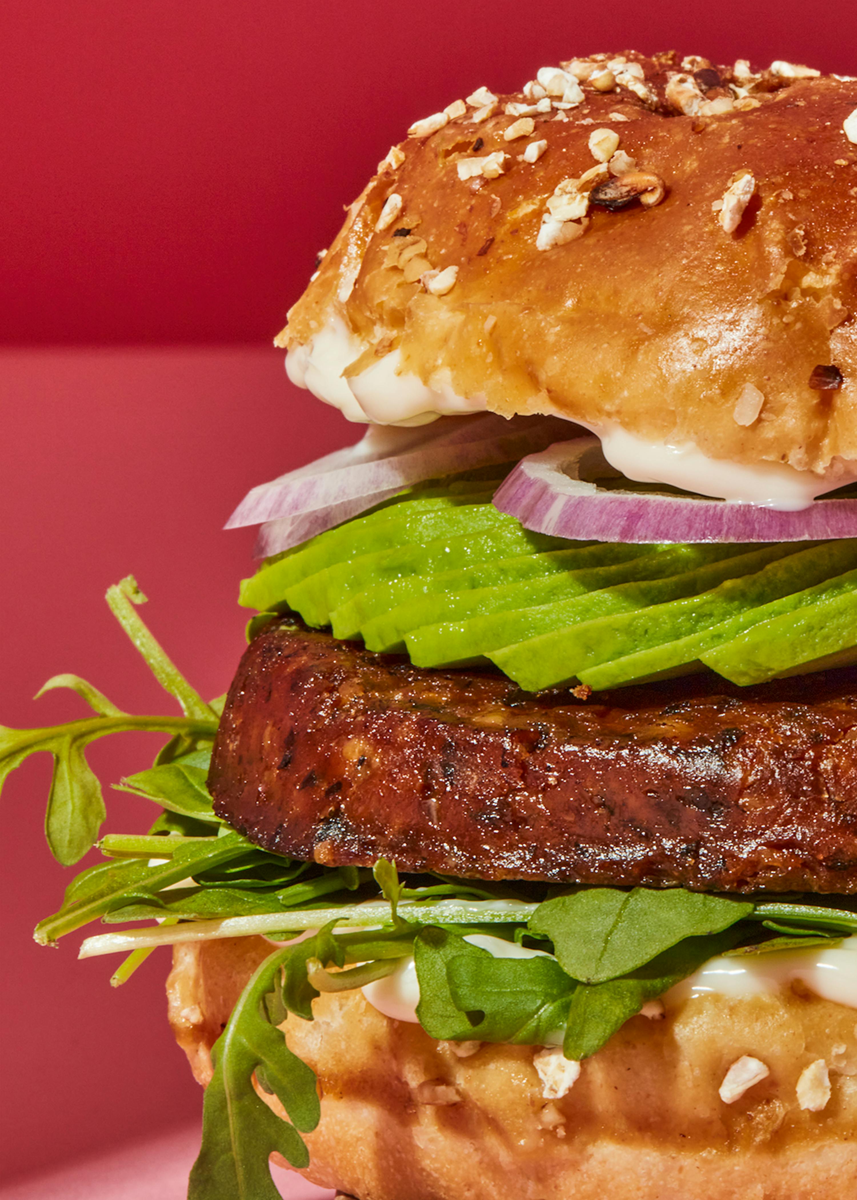 ein hamburger mit avocado und zwiebeln auf einem rosa hintergrund