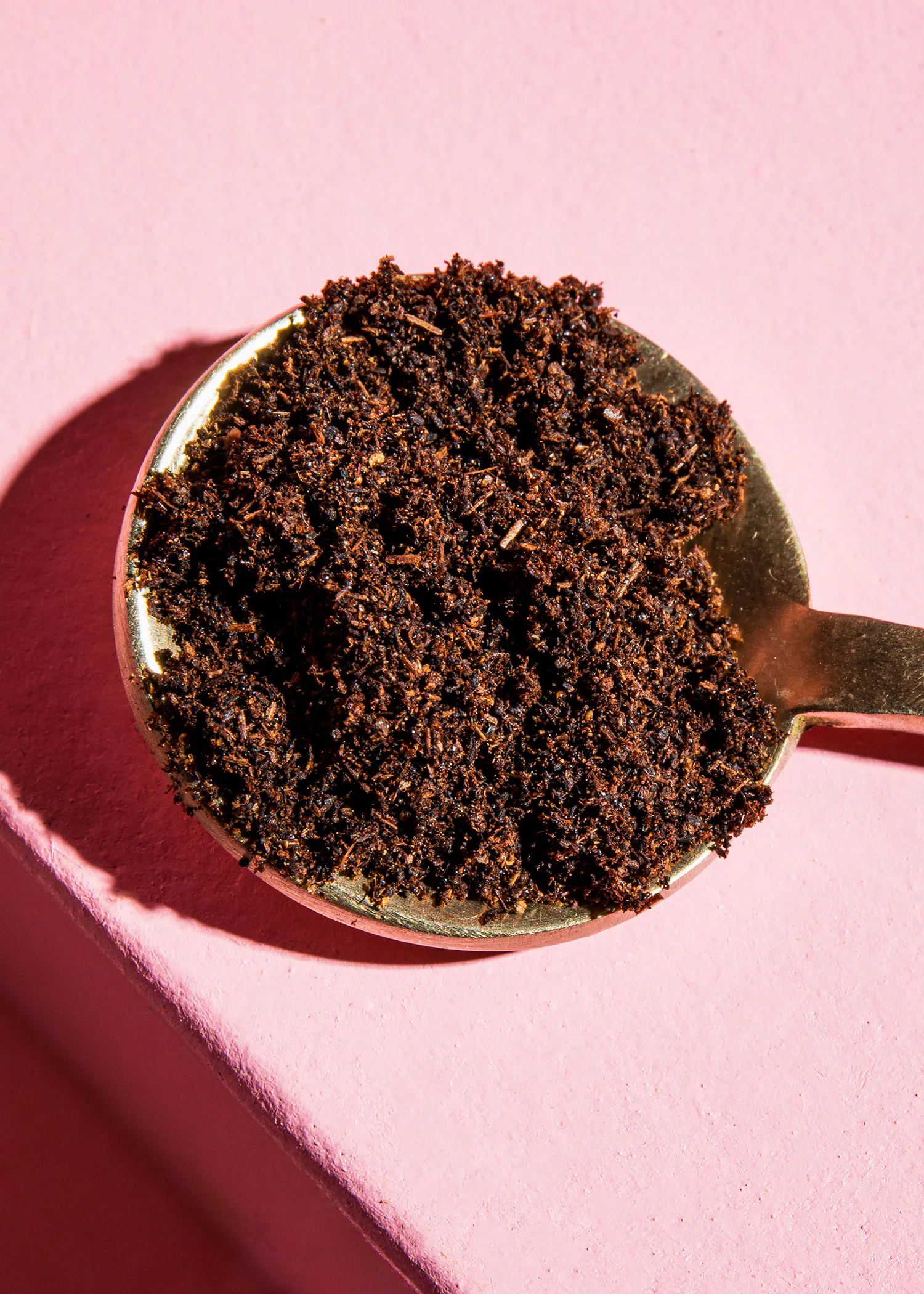 a gold measuring spoon filled with brown powder on a pink surface