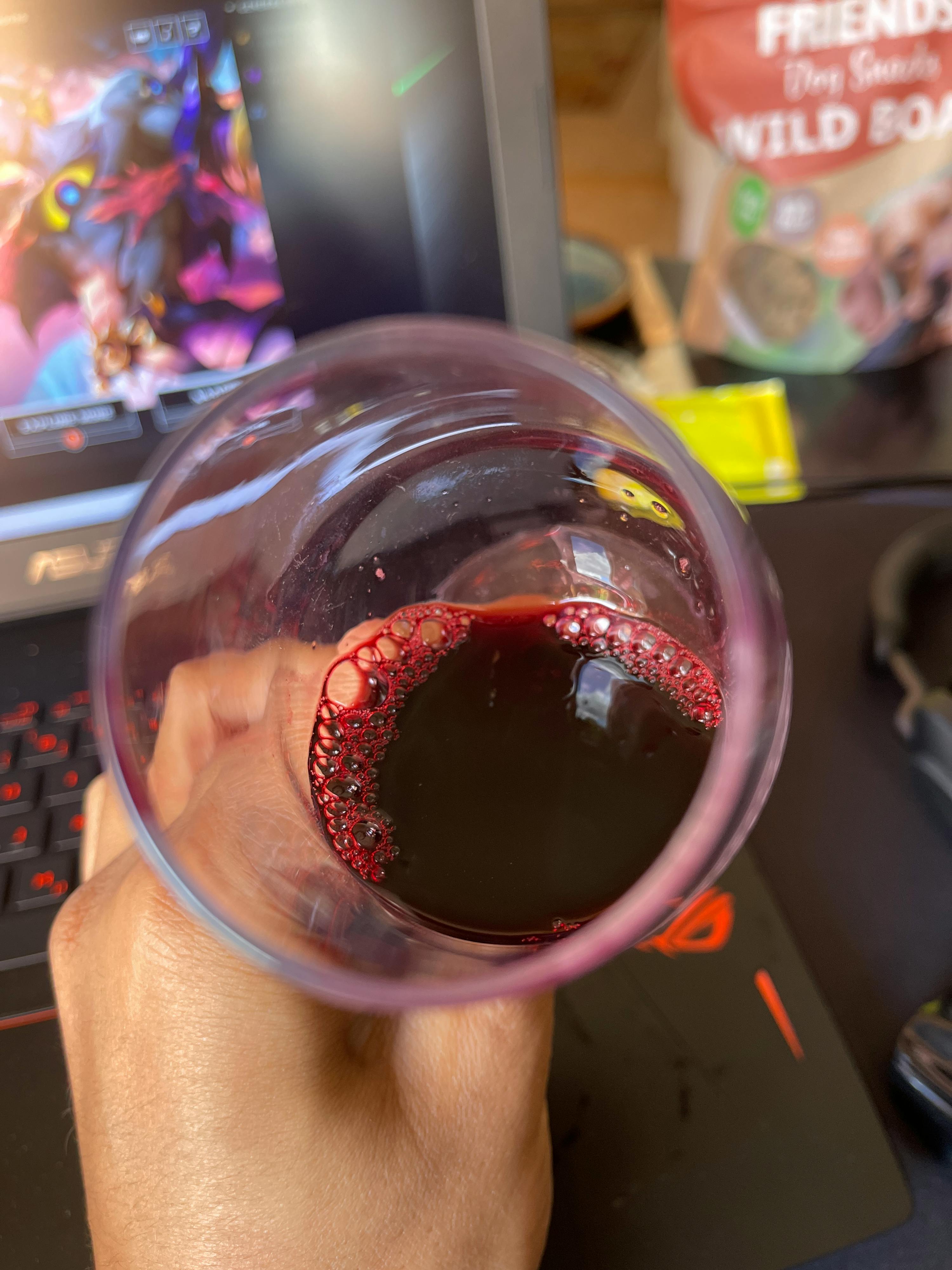 a person is holding a glass of wine in front of a laptop and a bag of friends dog treats
