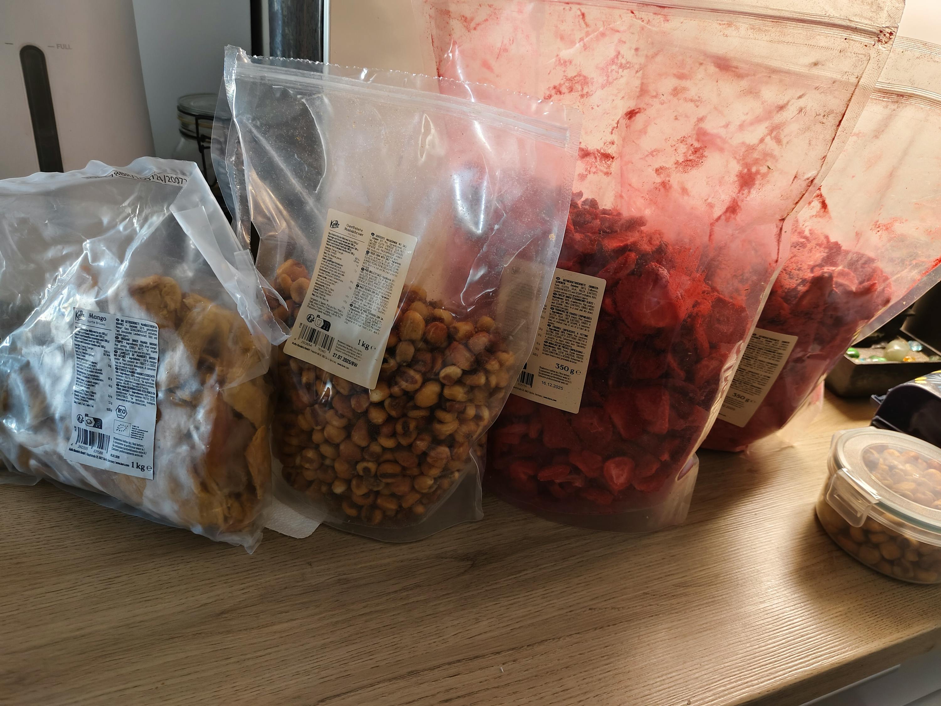 drei Plastiktüten mit Erdbeeren und Erdnüssen stehen auf einem Holztisch