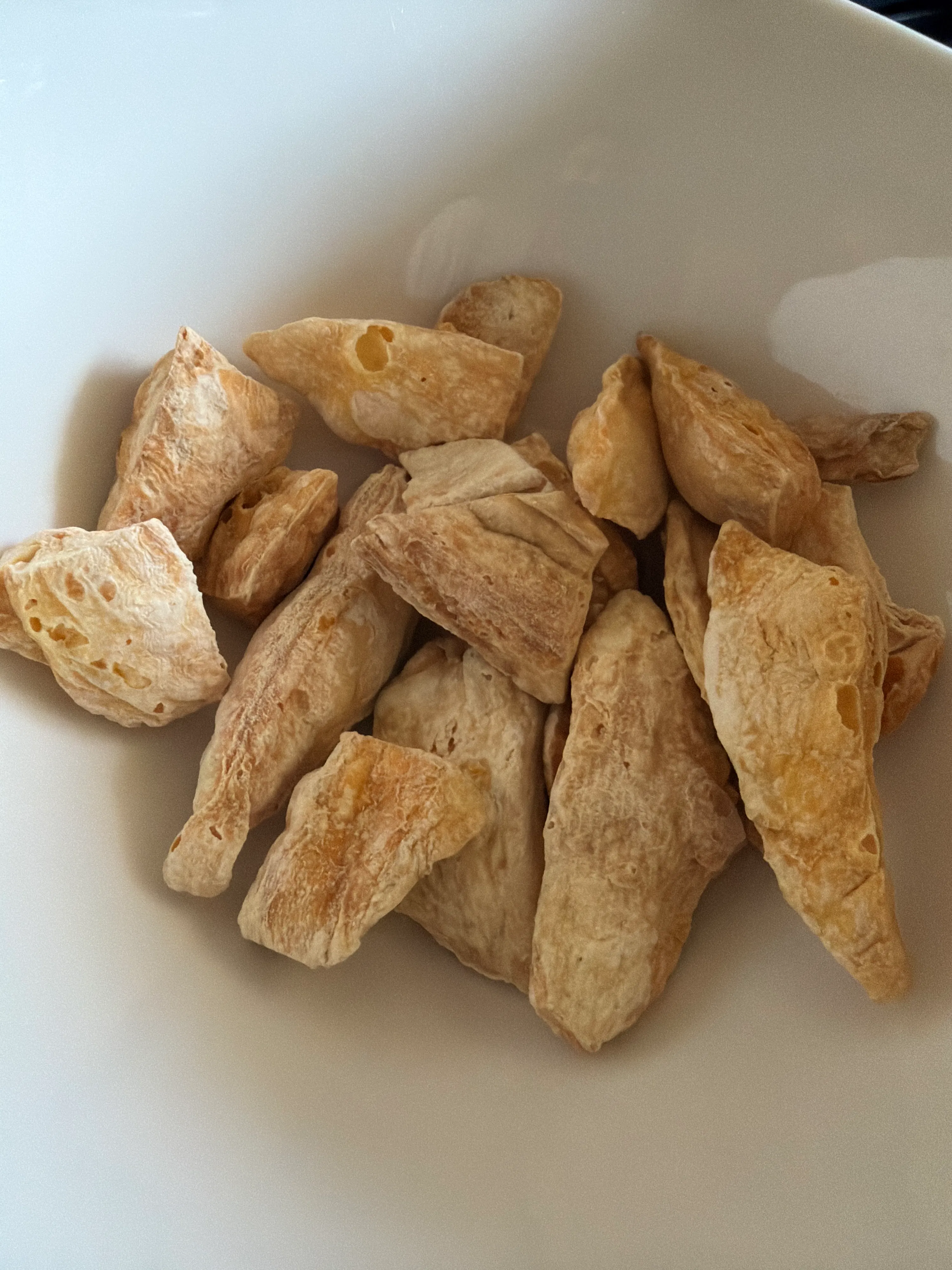 a white bowl filled with irregularly shaped, light brown, freeze-dried chicken pieces.