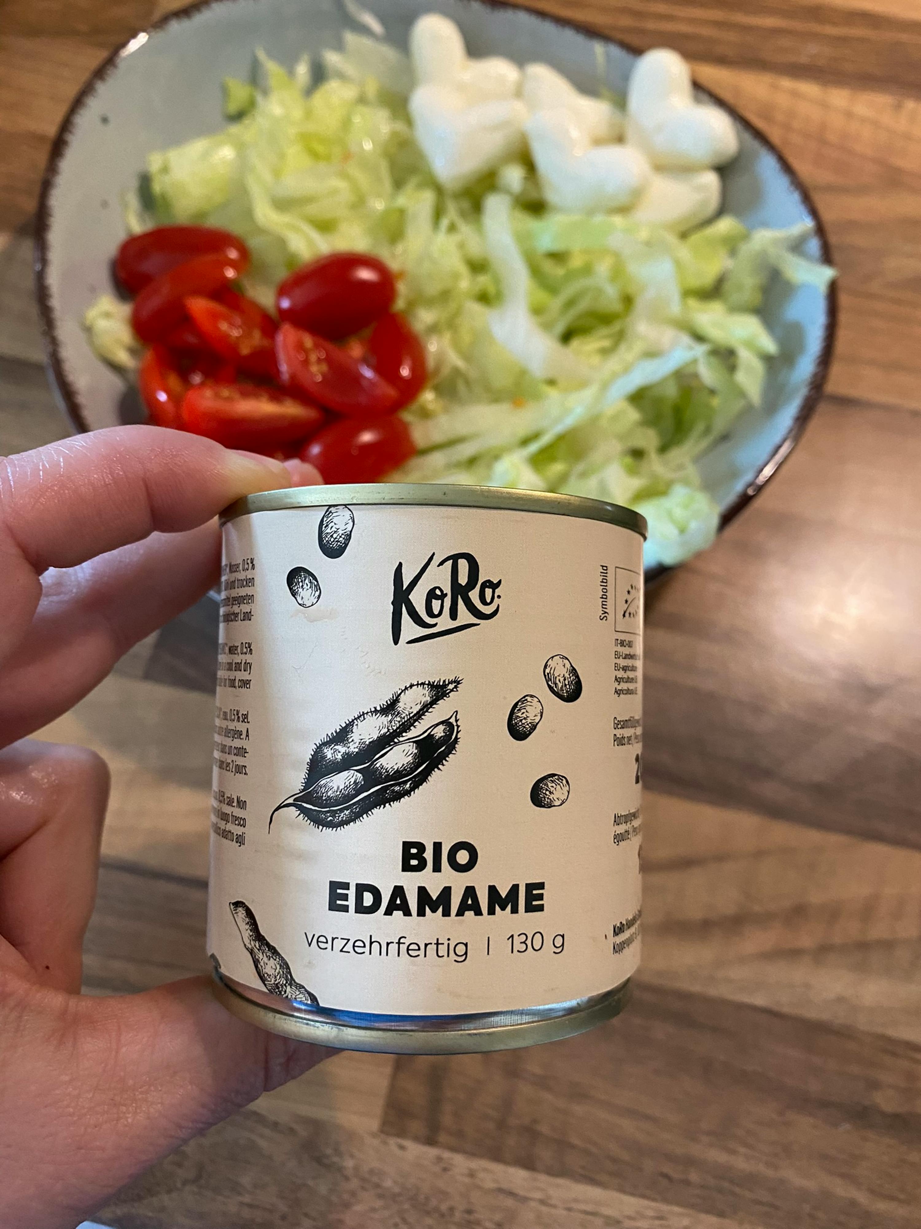 eine Person hält eine Dose Bio edamame vor einem Salat