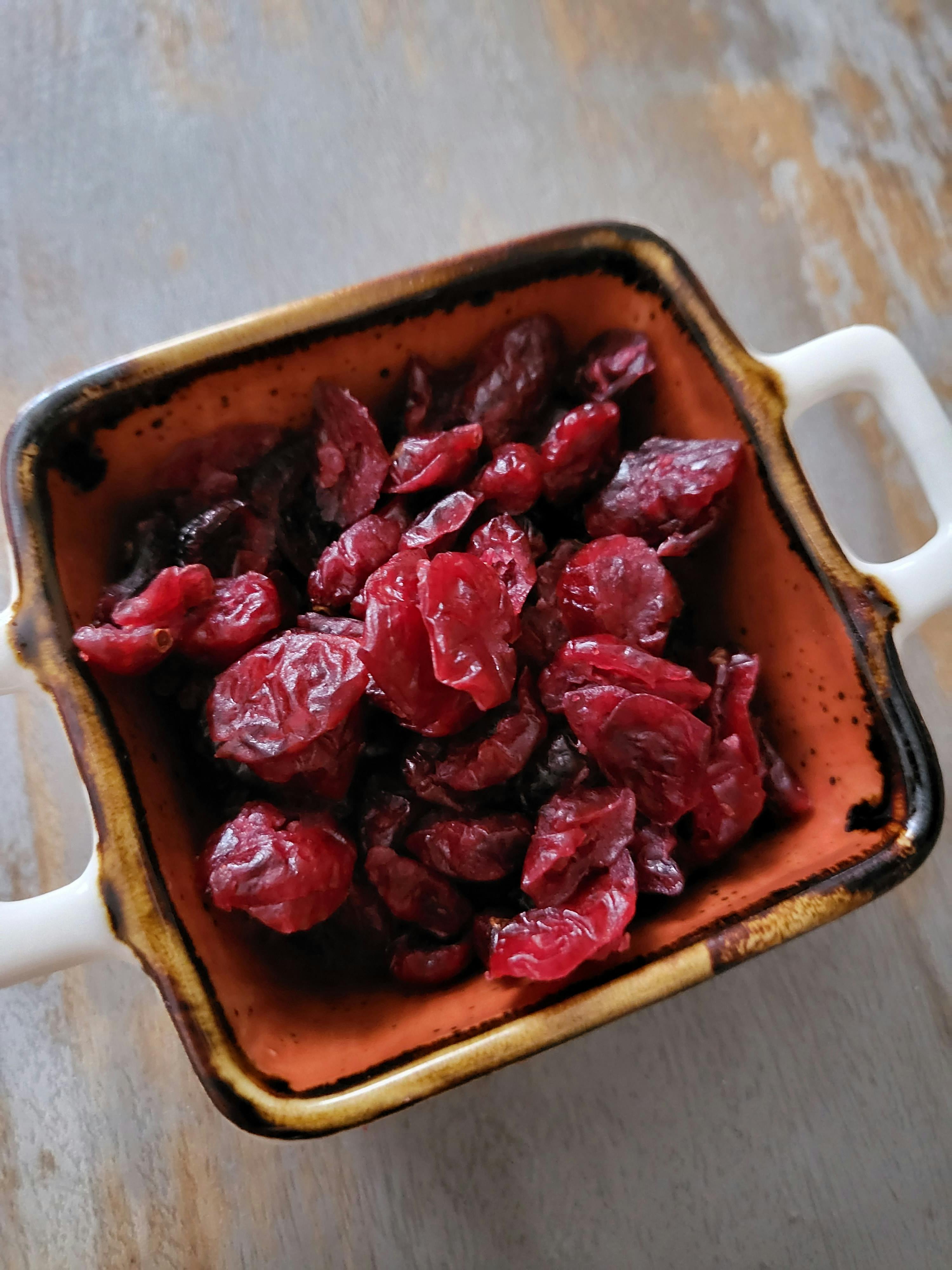 a bowl of dried cranberries sits on a wooden table