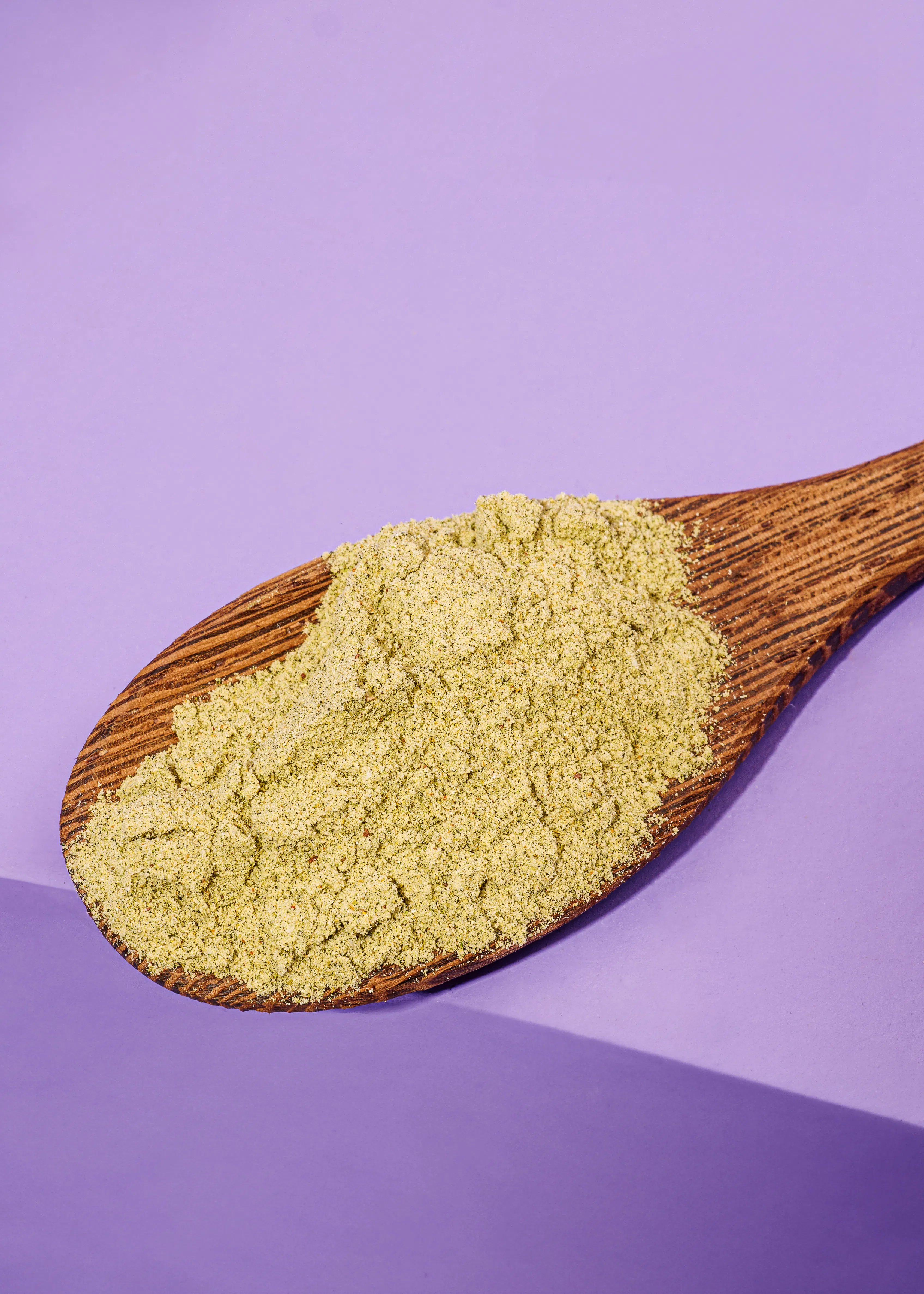 une cuillère en bois remplie de poudre verte sur un fond violet
