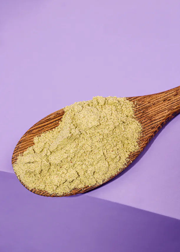 une cuillère en bois remplie de poudre verte sur un fond violet