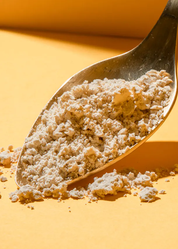 a metal spoon filled with powder on a yellow surface