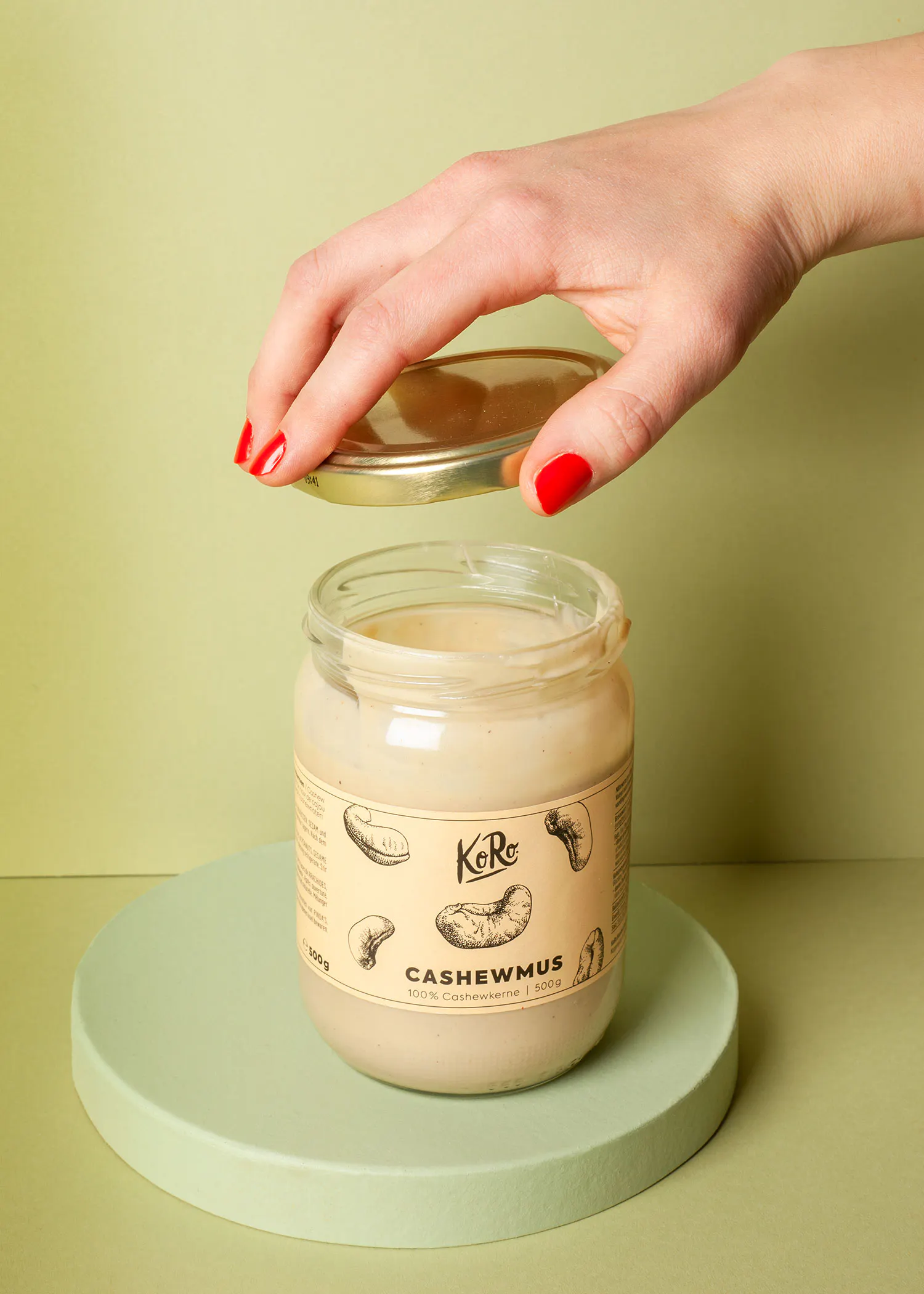 eine hand hält den deckel eines glases mit cashewmus