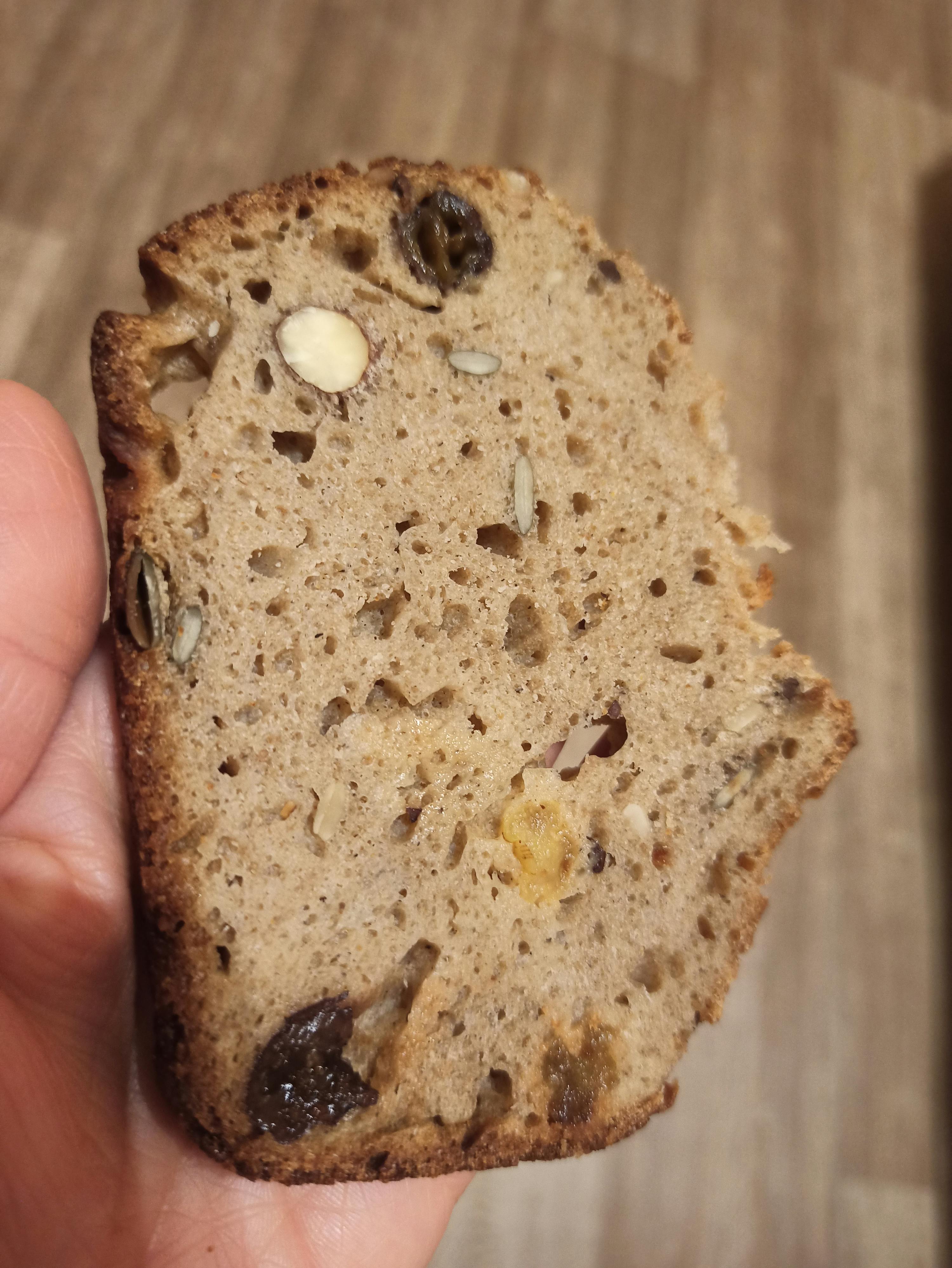 une personne tient une tranche de pain avec des noix et des raisins