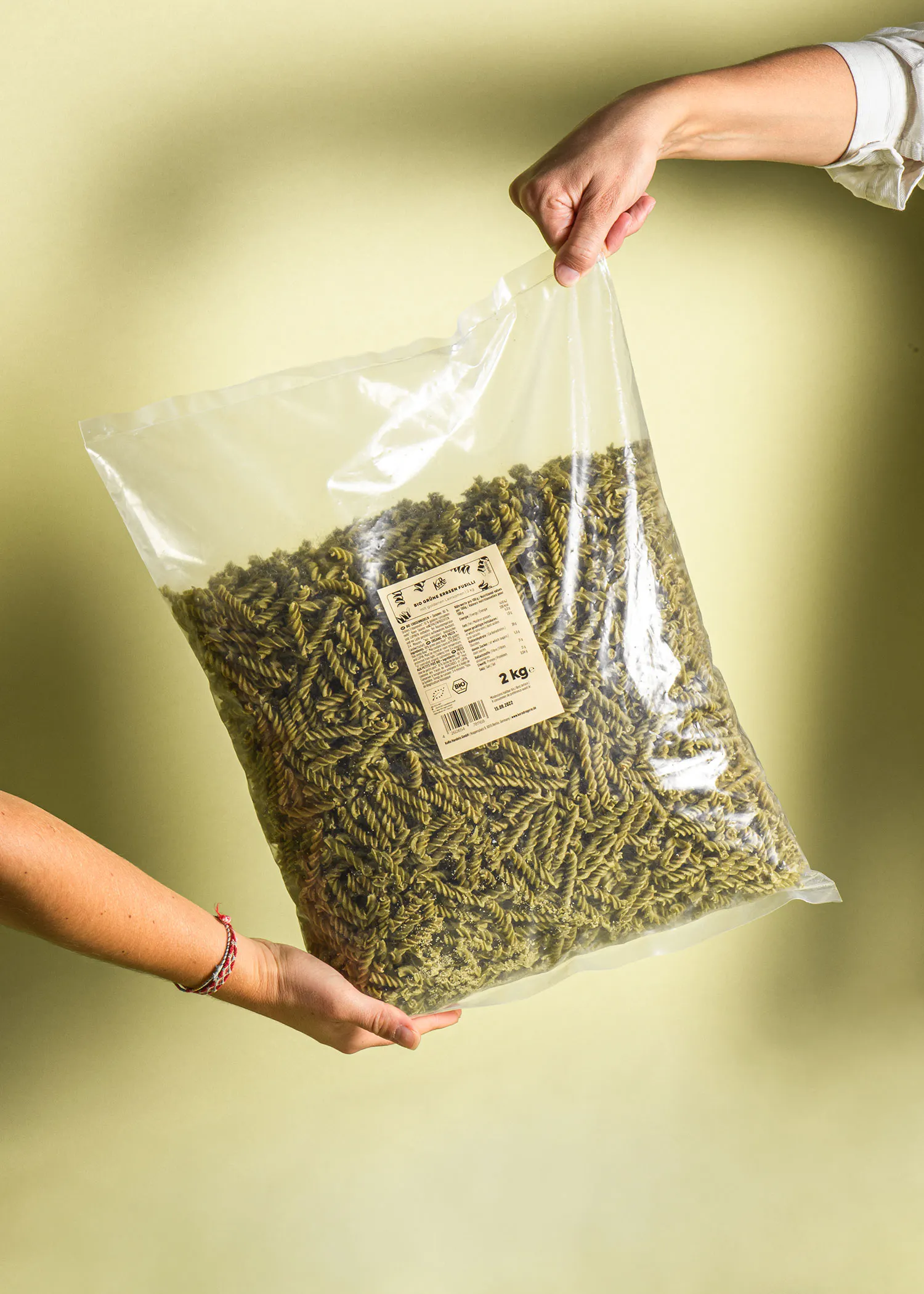 eine Person hält eine Plastiktüte mit grünen Nudeln in ihren Händen