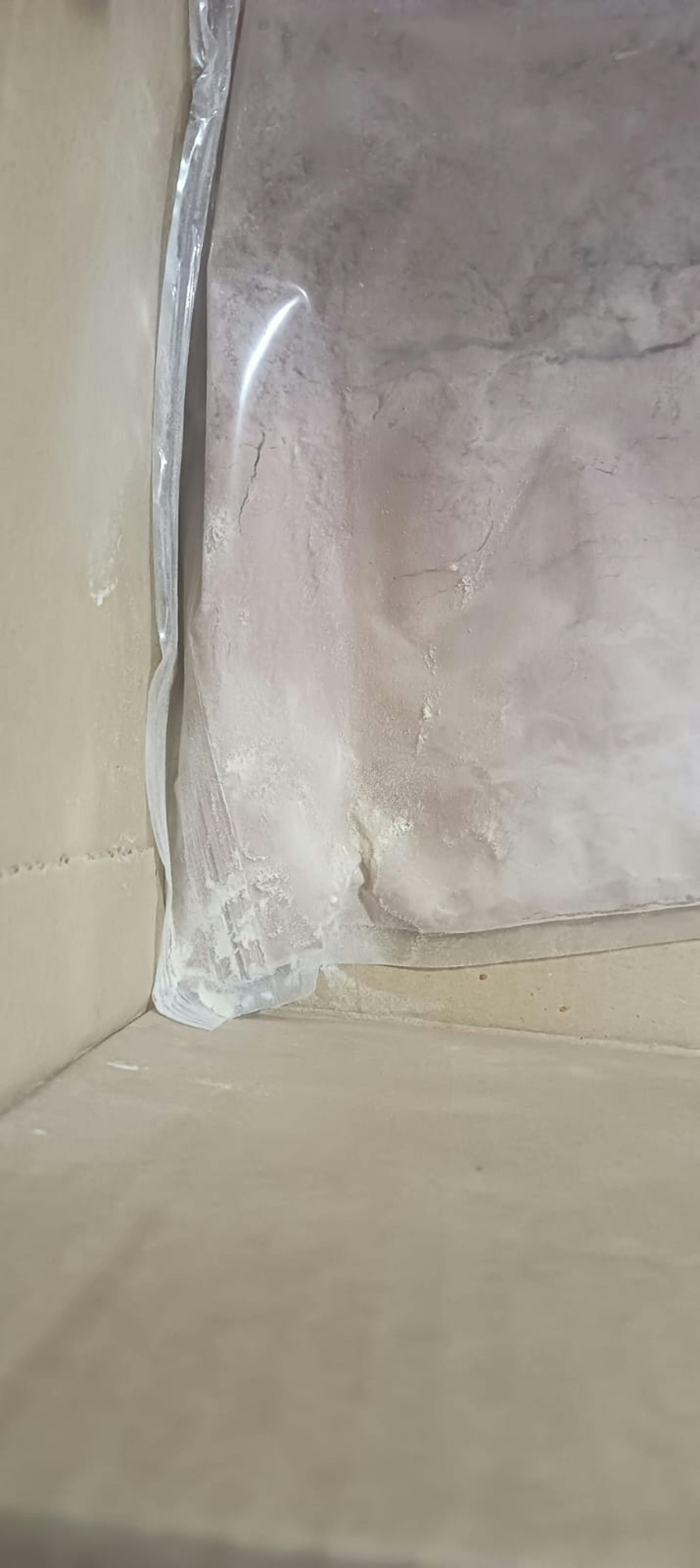 un sac en plastique transparent rempli de poudre claire est posé dans une boîte en carton, avec un peu de poudre répandue dans le coin.