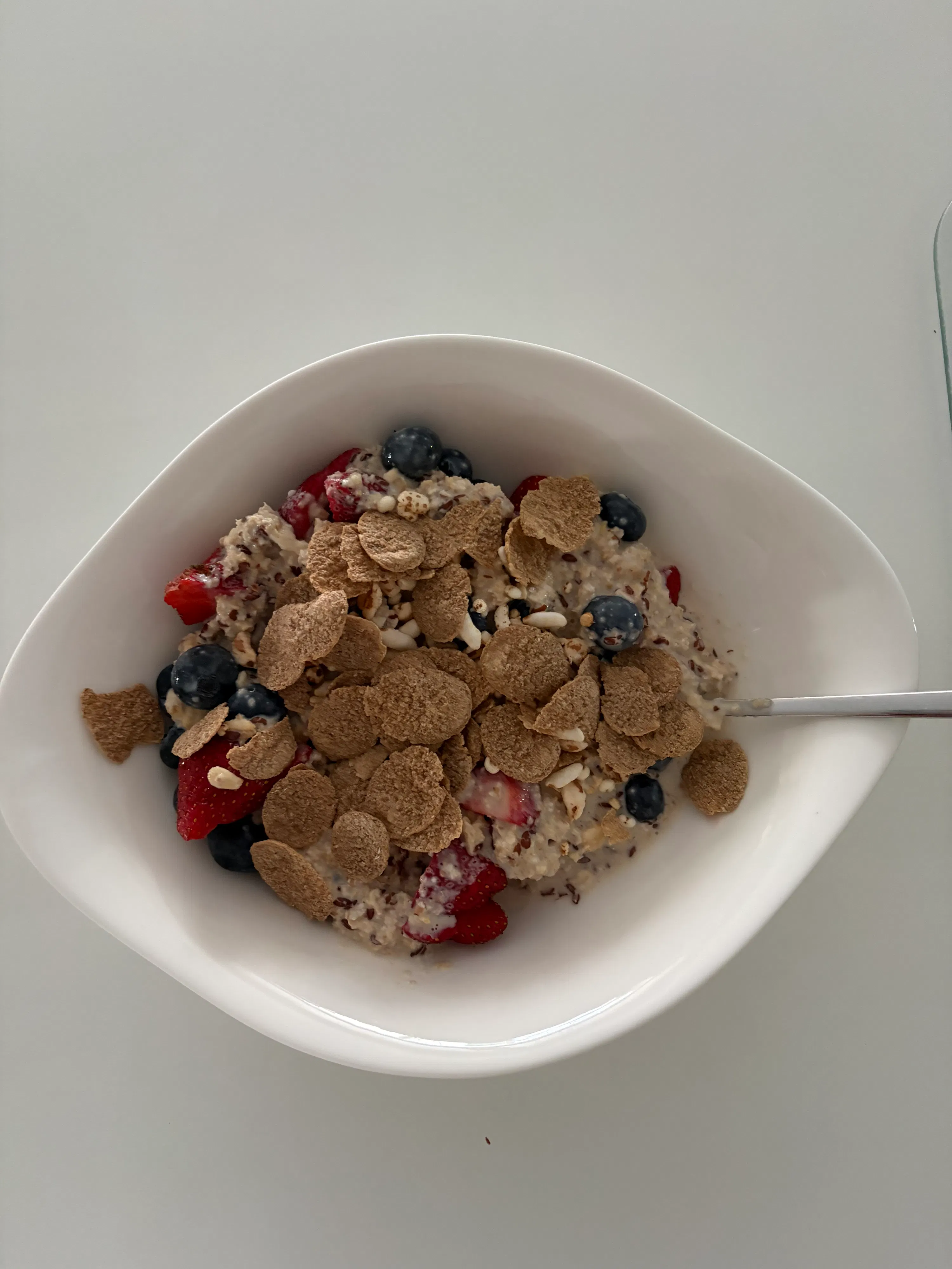 eine weiße schale mit haferbrei, garniert mit blaubeeren, erdbeeren und herzförmigen cornflakes.
