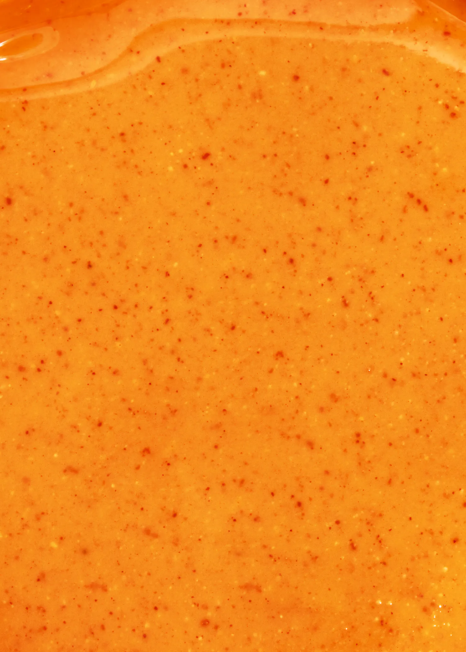 un gros plan d' une sauce orange avec des graines rouges