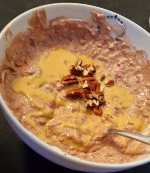 a bowl of food with pecans and cheese and a spoon