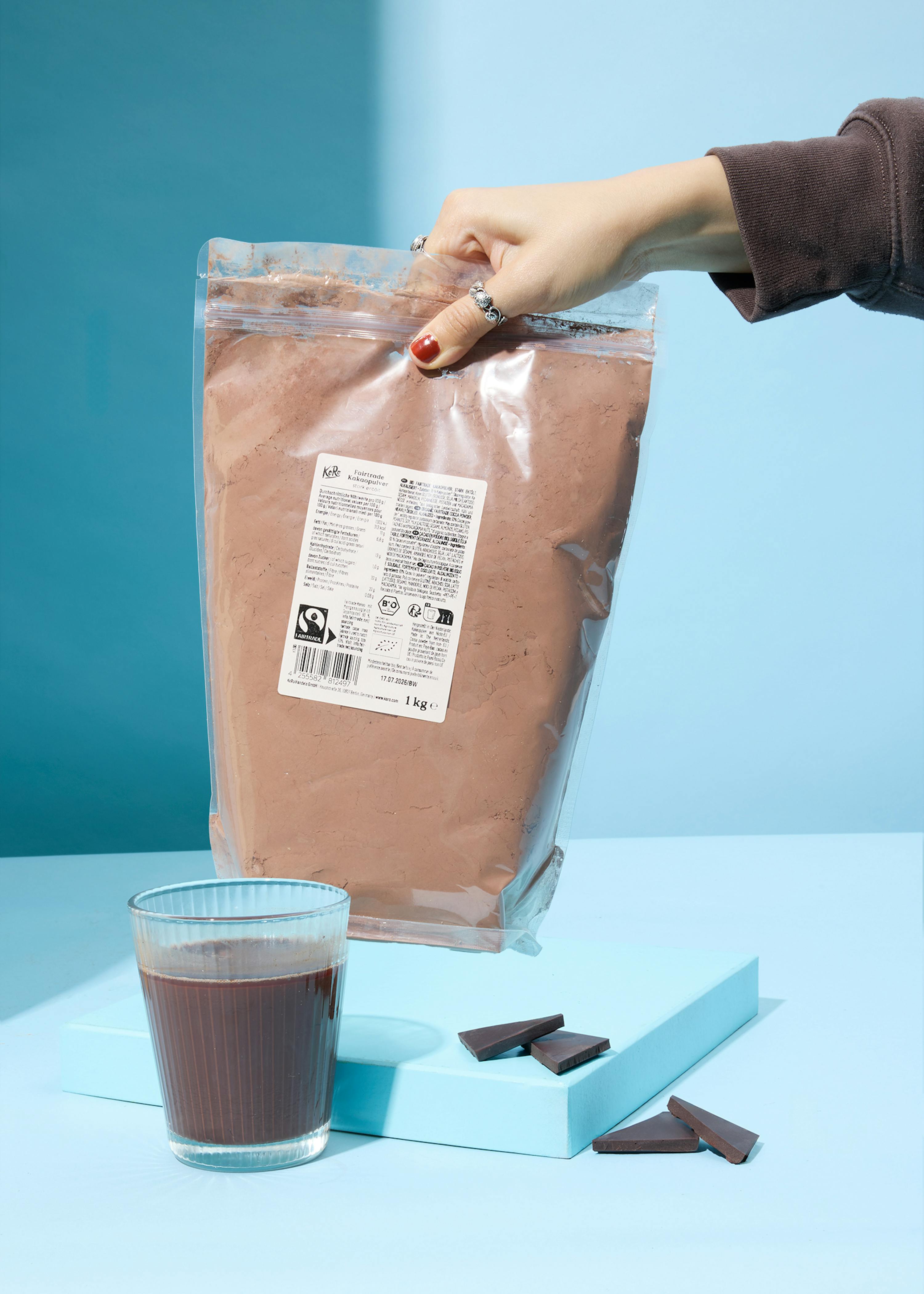 a person holding a bag of cocoa powder next to a glass of cocoa