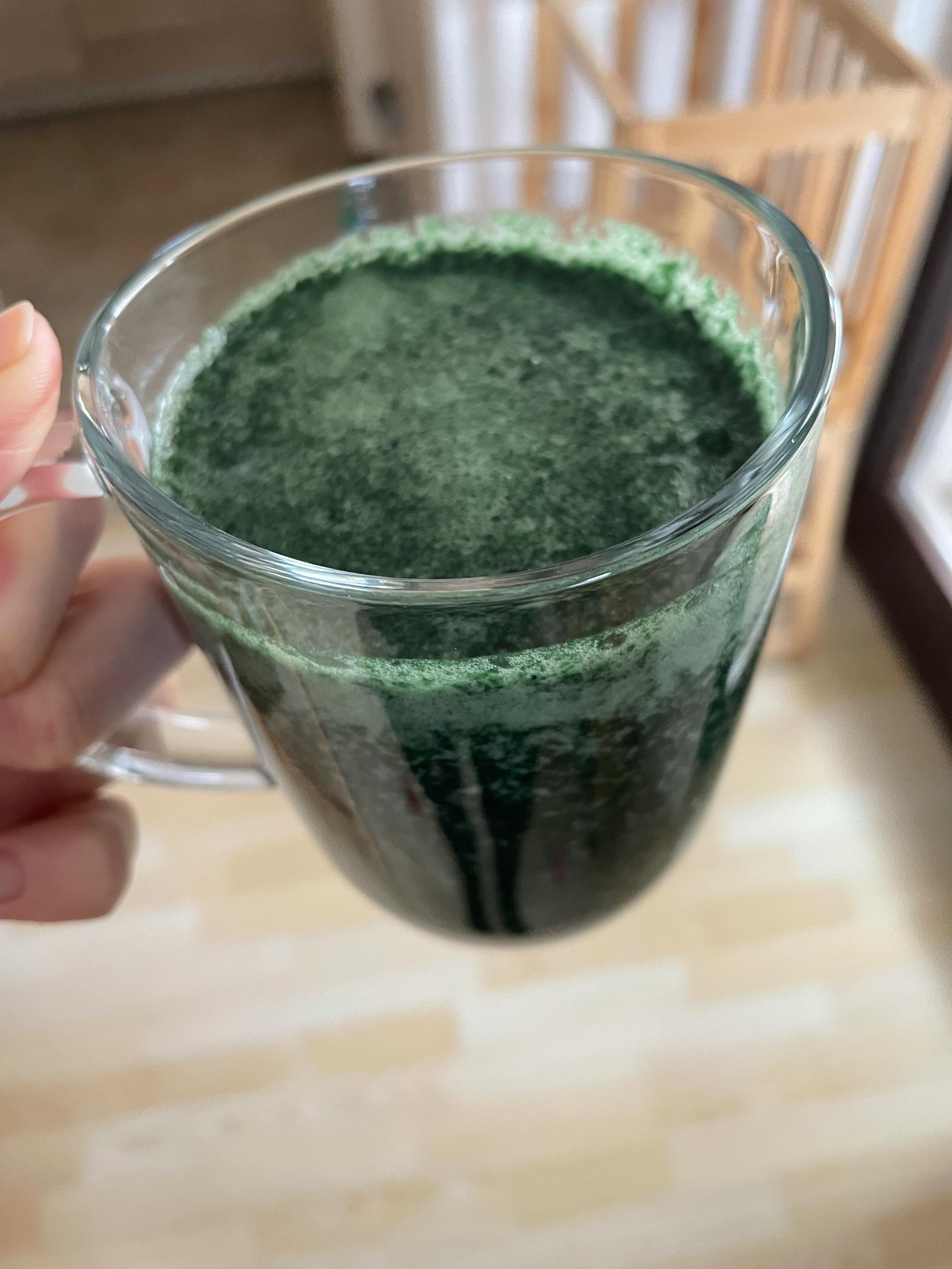 eine Person hält ein Glas mit grünem Getränk darin