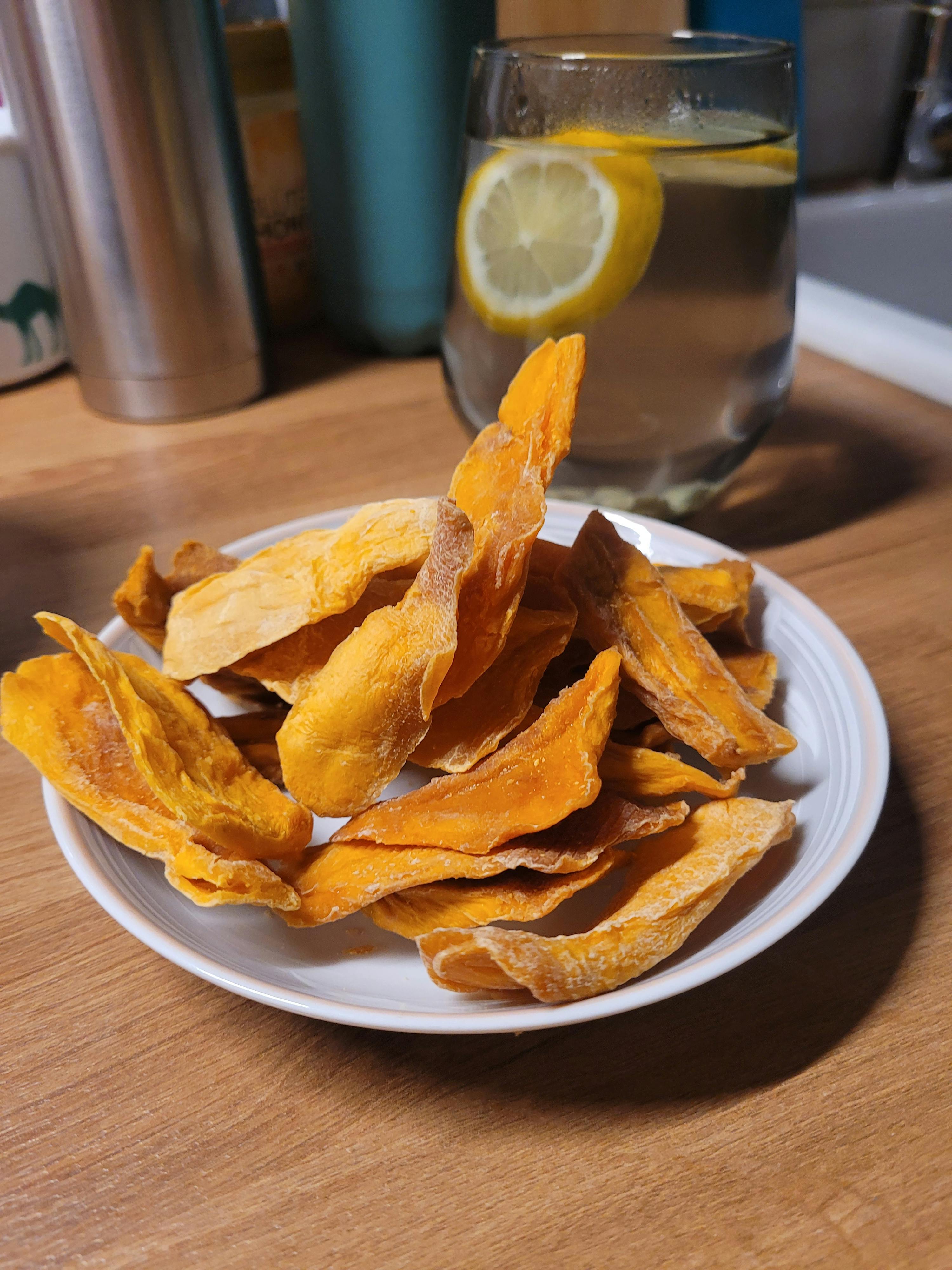 ein weißer Teller mit getrockneten Äpfeln steht auf einem Holztisch neben einem Glas Wasser mit einer Limettenscheibe darin