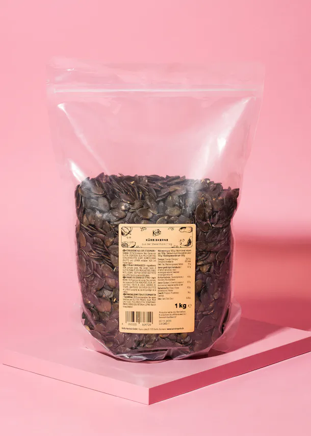 un sac en plastique rempli de graines de citrouille sur une table rose