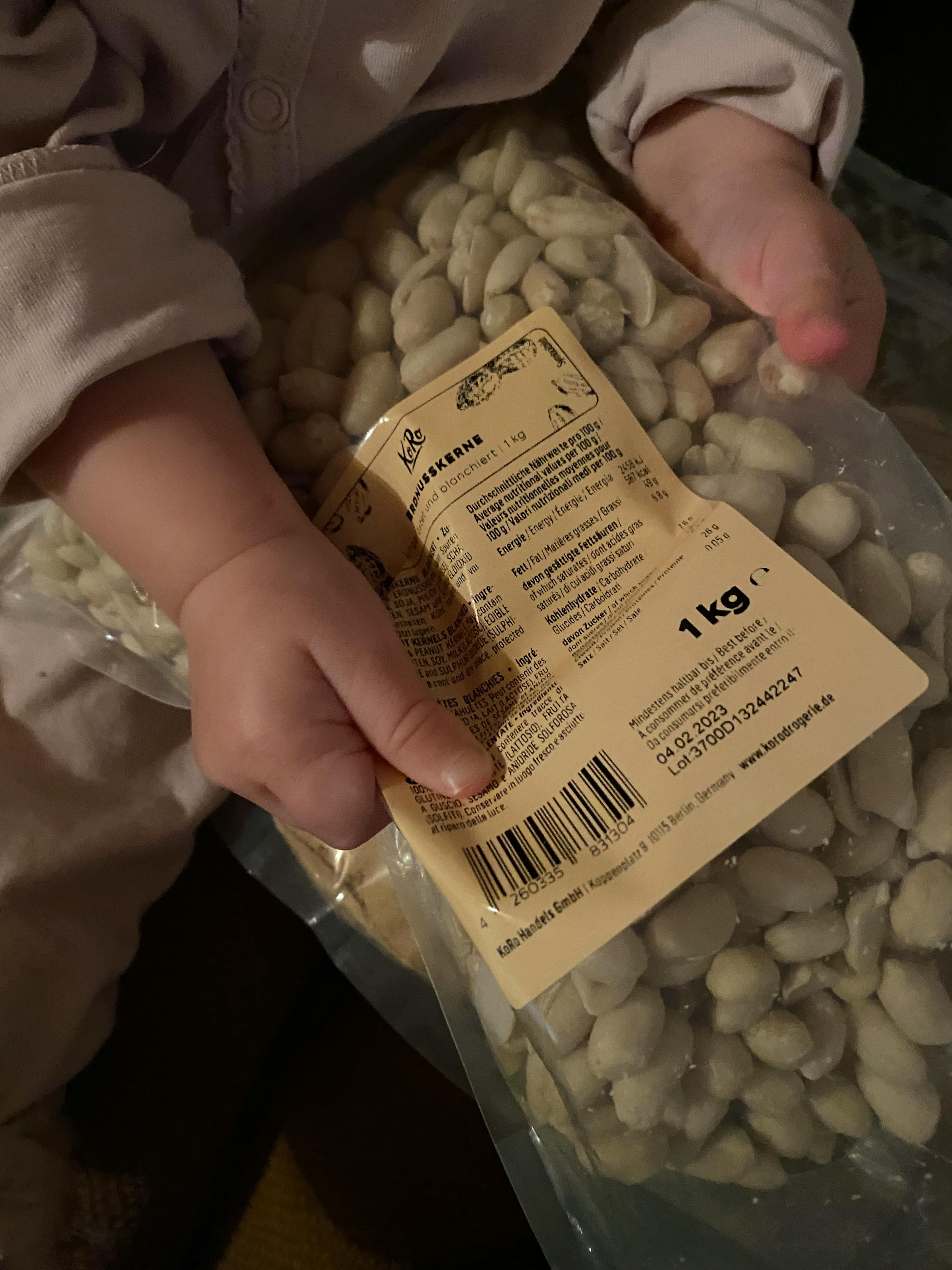 ein Baby hält einen Plastikbeutel mit 1 kg Bohnen in seinen Händen