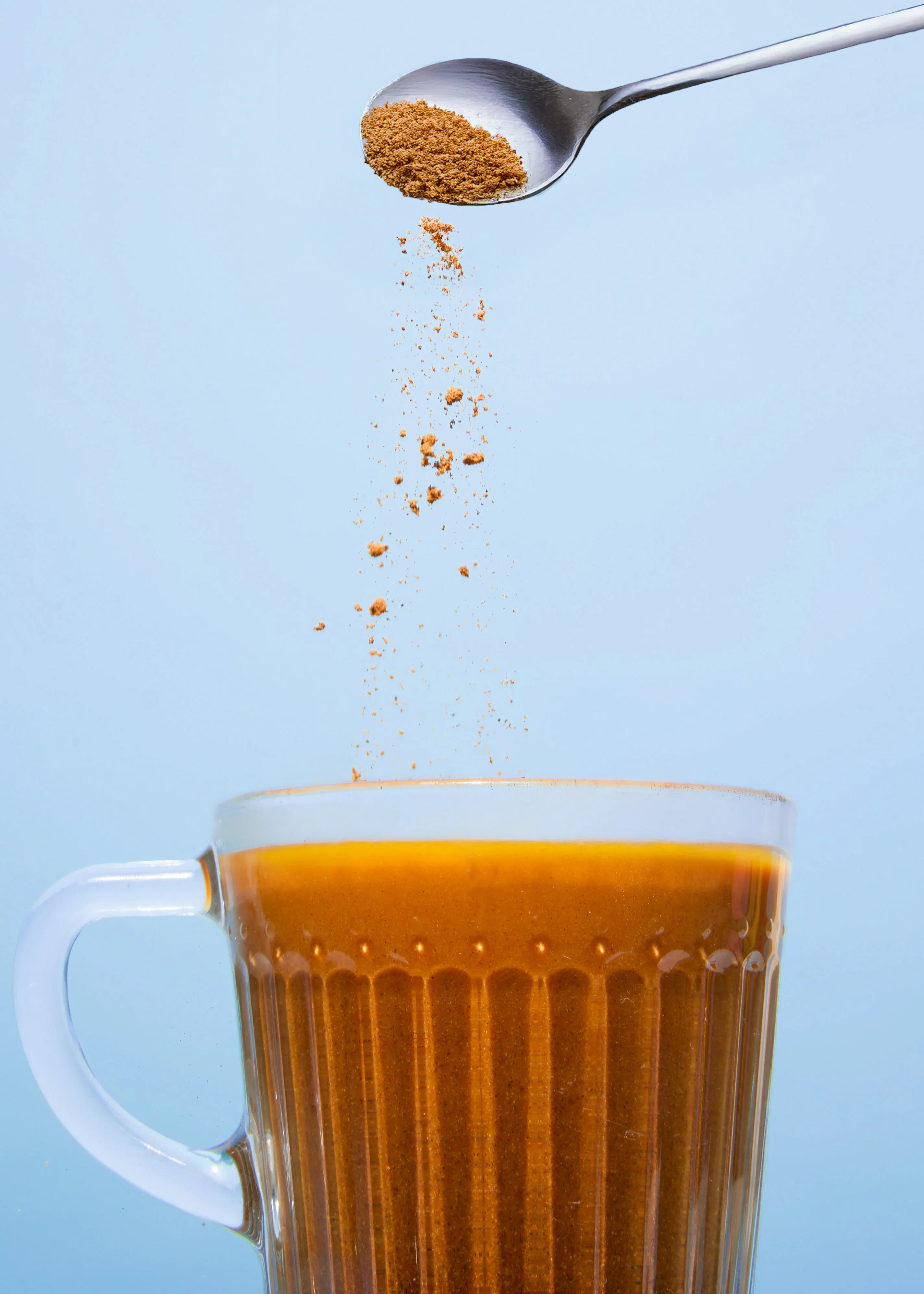 une cuillère remplie de poudre de café est versée dans une tasse de café