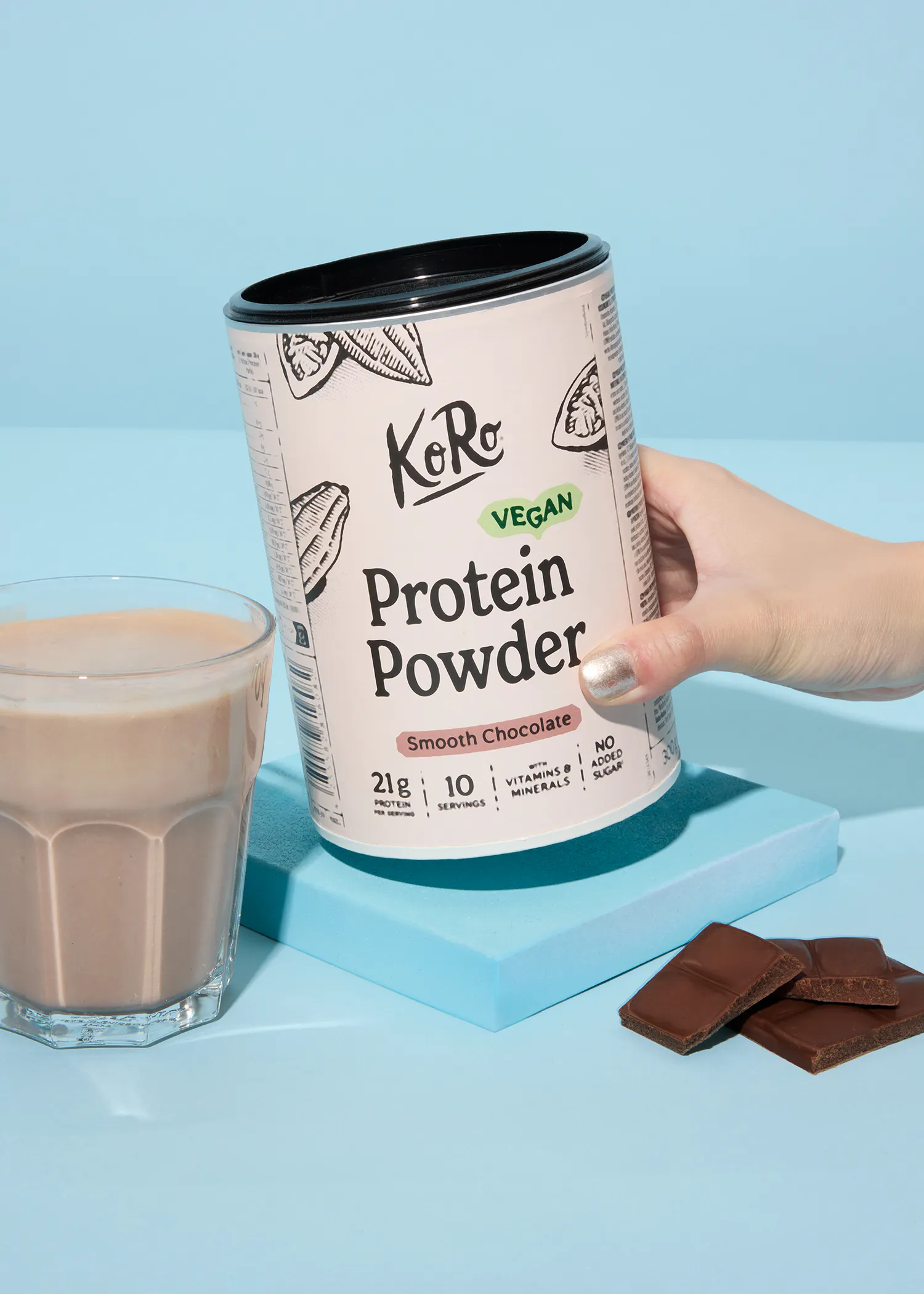 une personne tient une boîte de poudre de protéines à côté d' un verre de chocolat