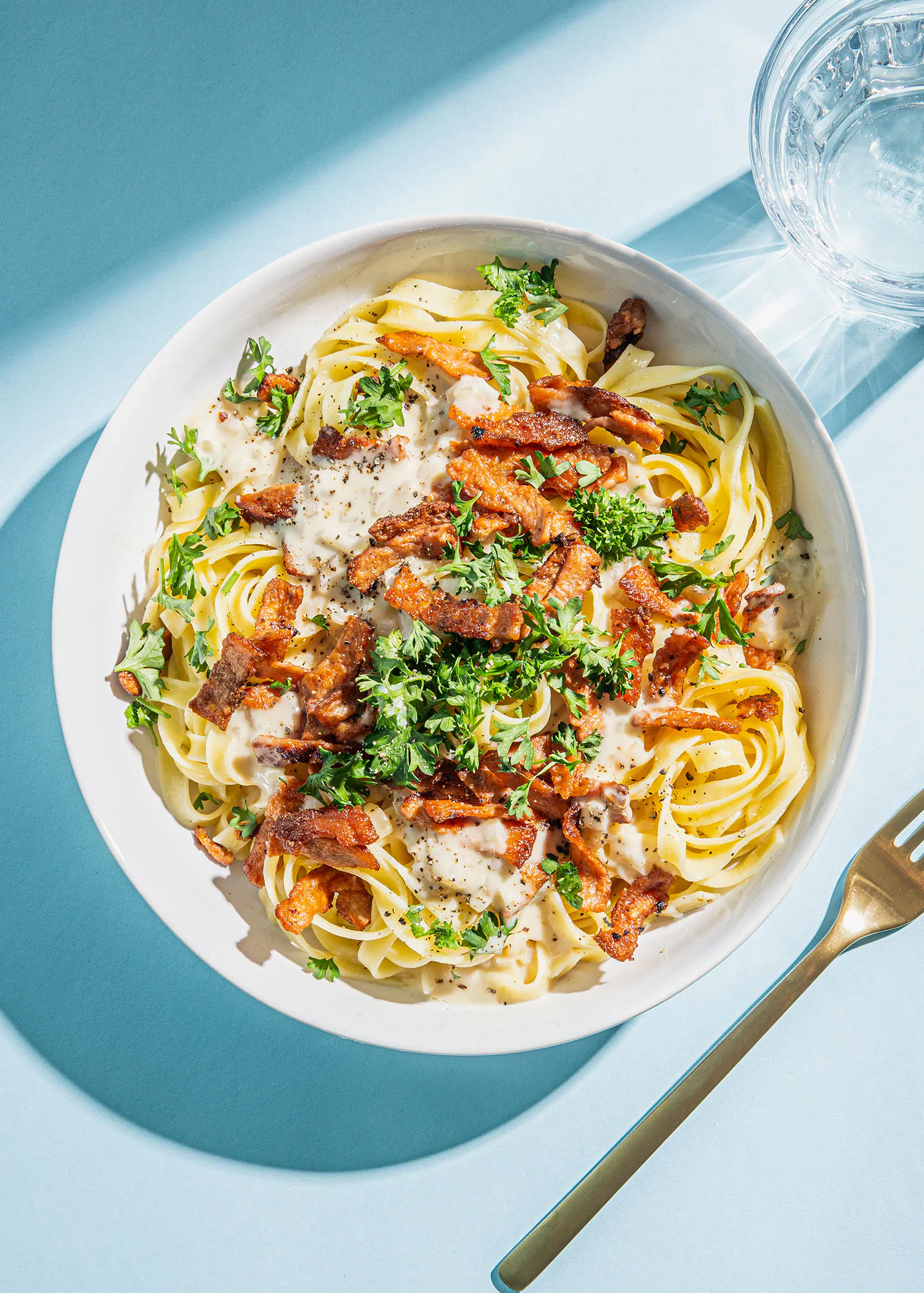a white bowl filled with noodles and bacon next to a fork