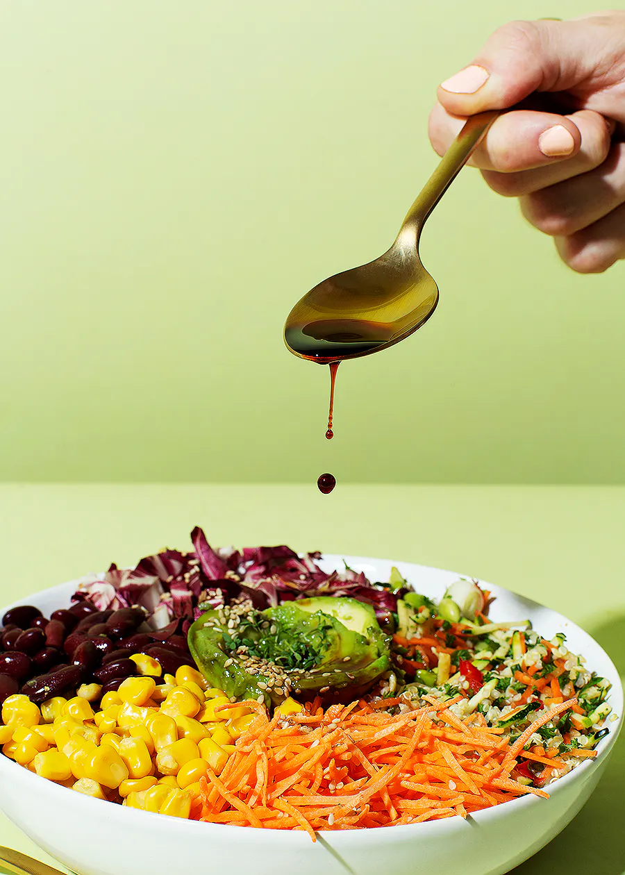 eine Person gießt Soße auf einen Salat mit einem Löffel