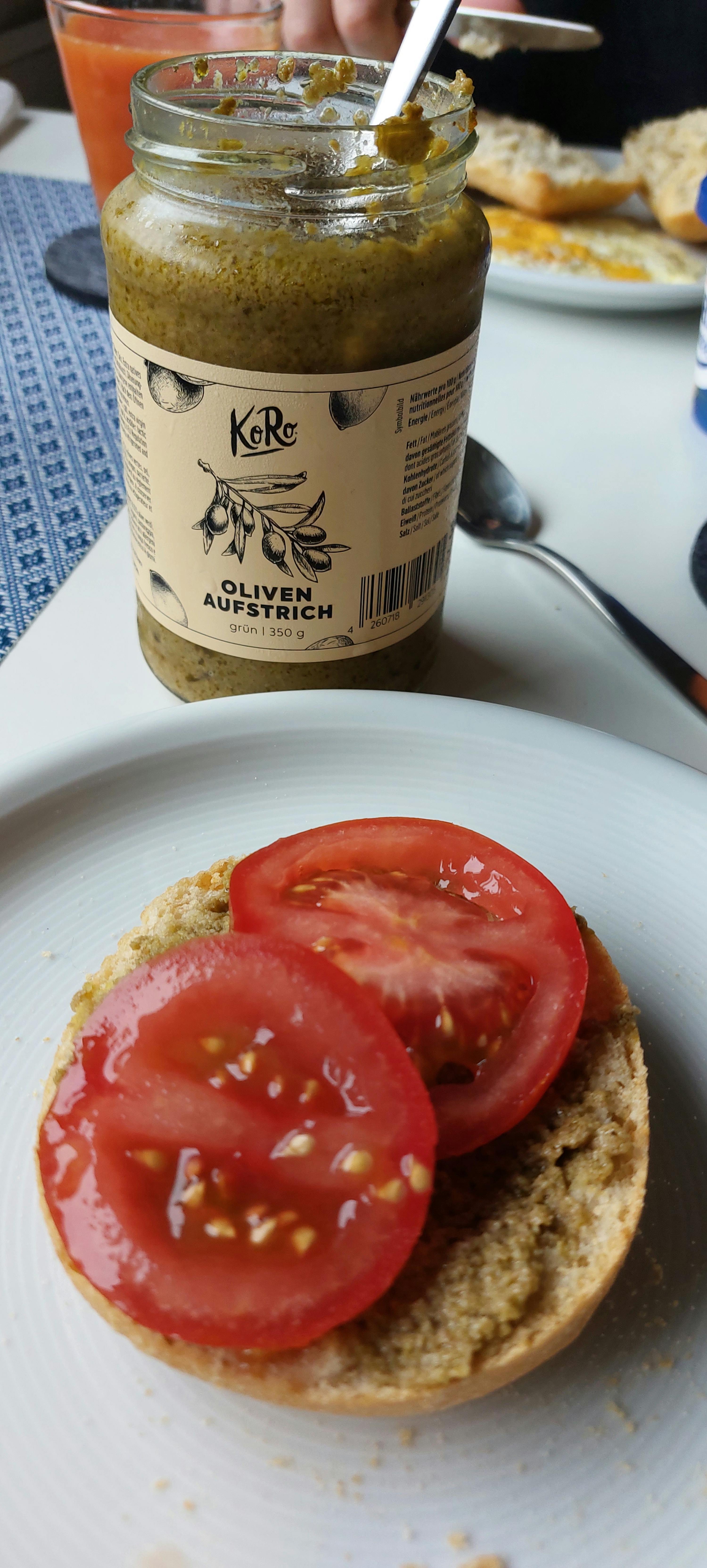 a sandwich with tomatoes and a jar of koro olive aufstrich