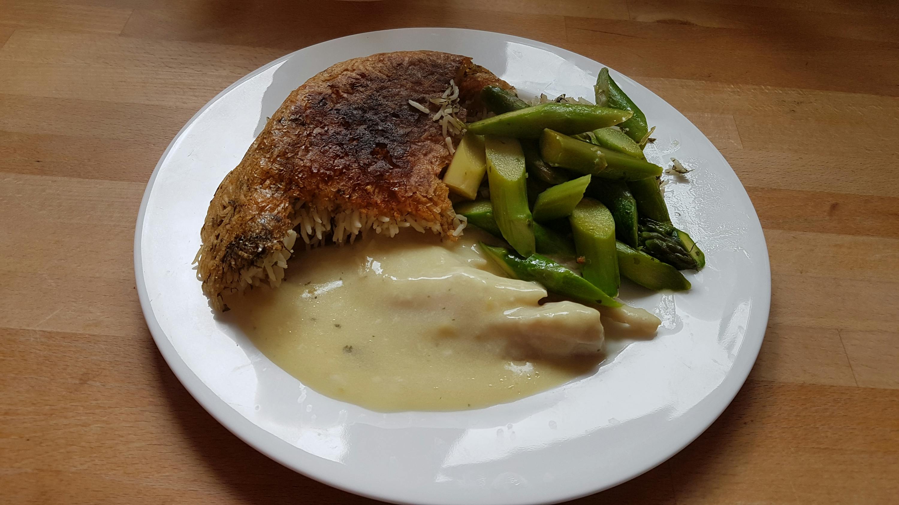 a plate of food with asparagus and sauce on a wooden table