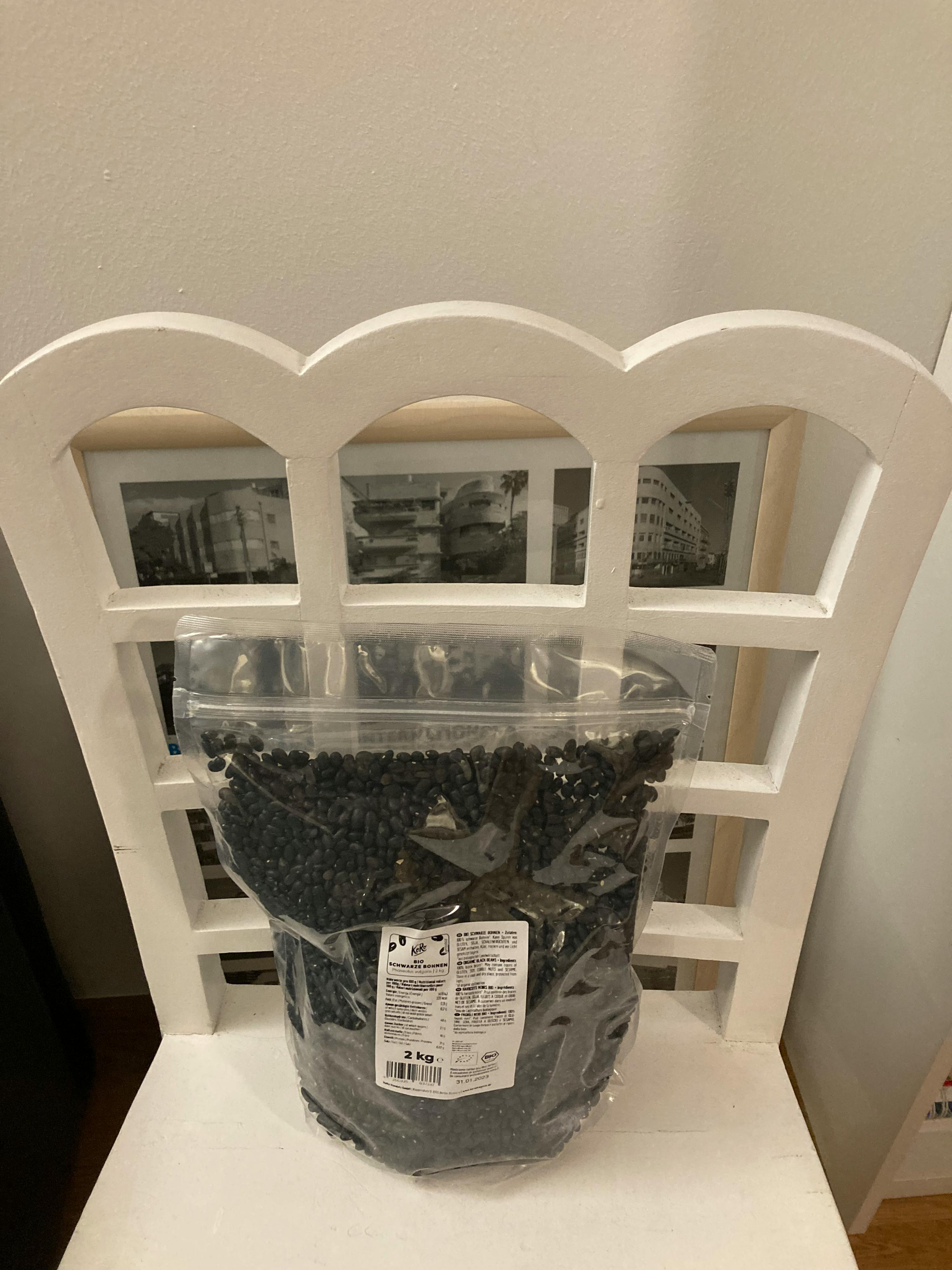 eine Tüte schwarze Bohnen steht auf einem weißen Regal