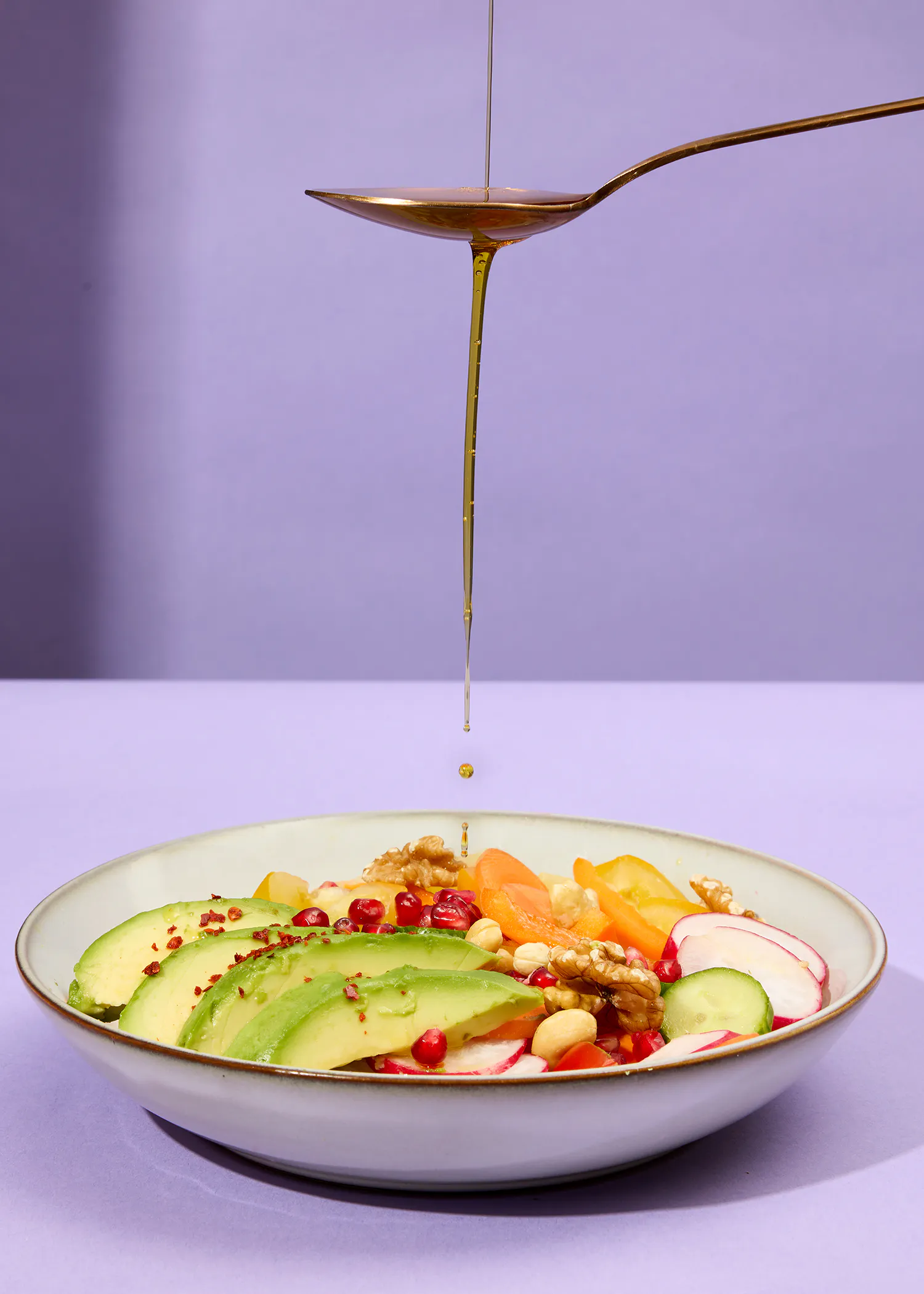 ein Löffel gibt Öl über einen Salat mit Avocado und Nüssen