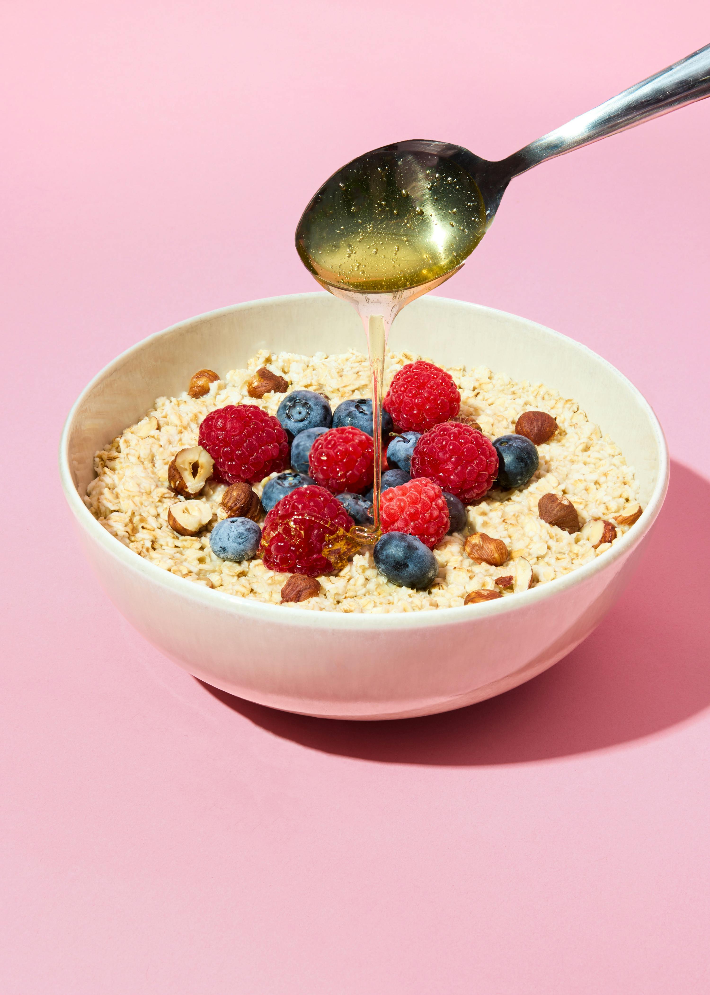 una ciotola di farina d' avena con lamponi e mirtilli e un cucchiaio di sciroppo