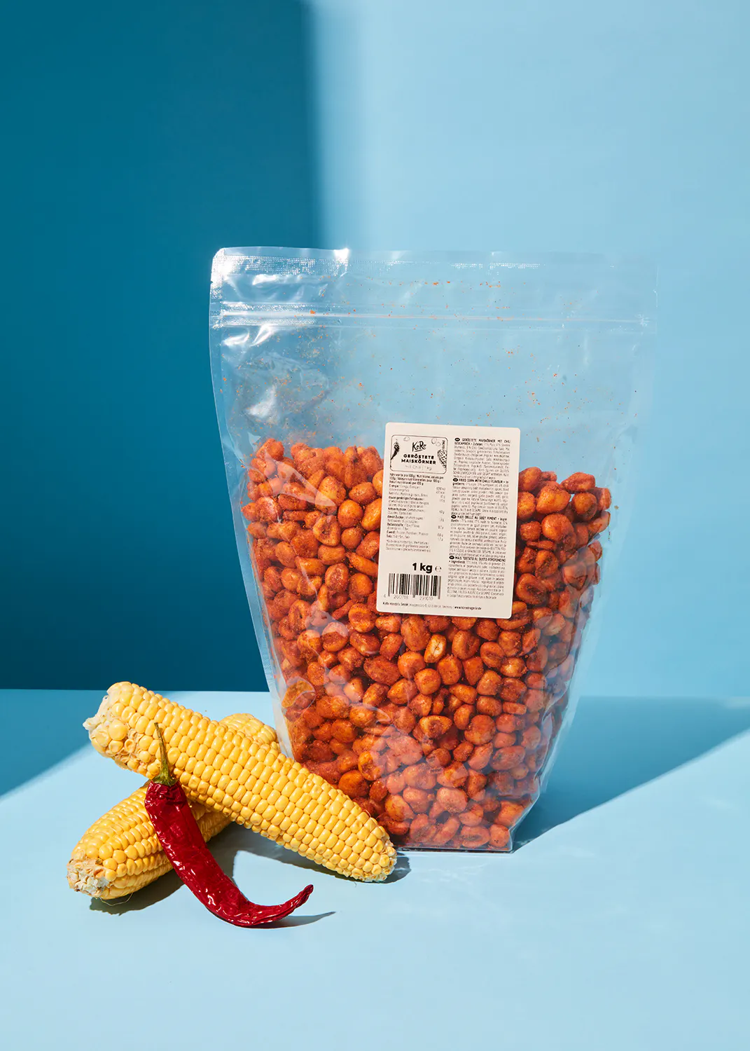 un sac de maïs épicé est assis sur une table bleue à côté d' une épi de maïs et d' un piment rouge