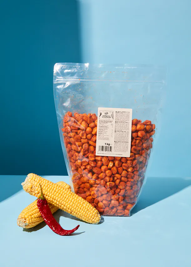 un sac de maïs épicé est assis sur une table bleue à côté d' une épi de maïs et d' un piment rouge