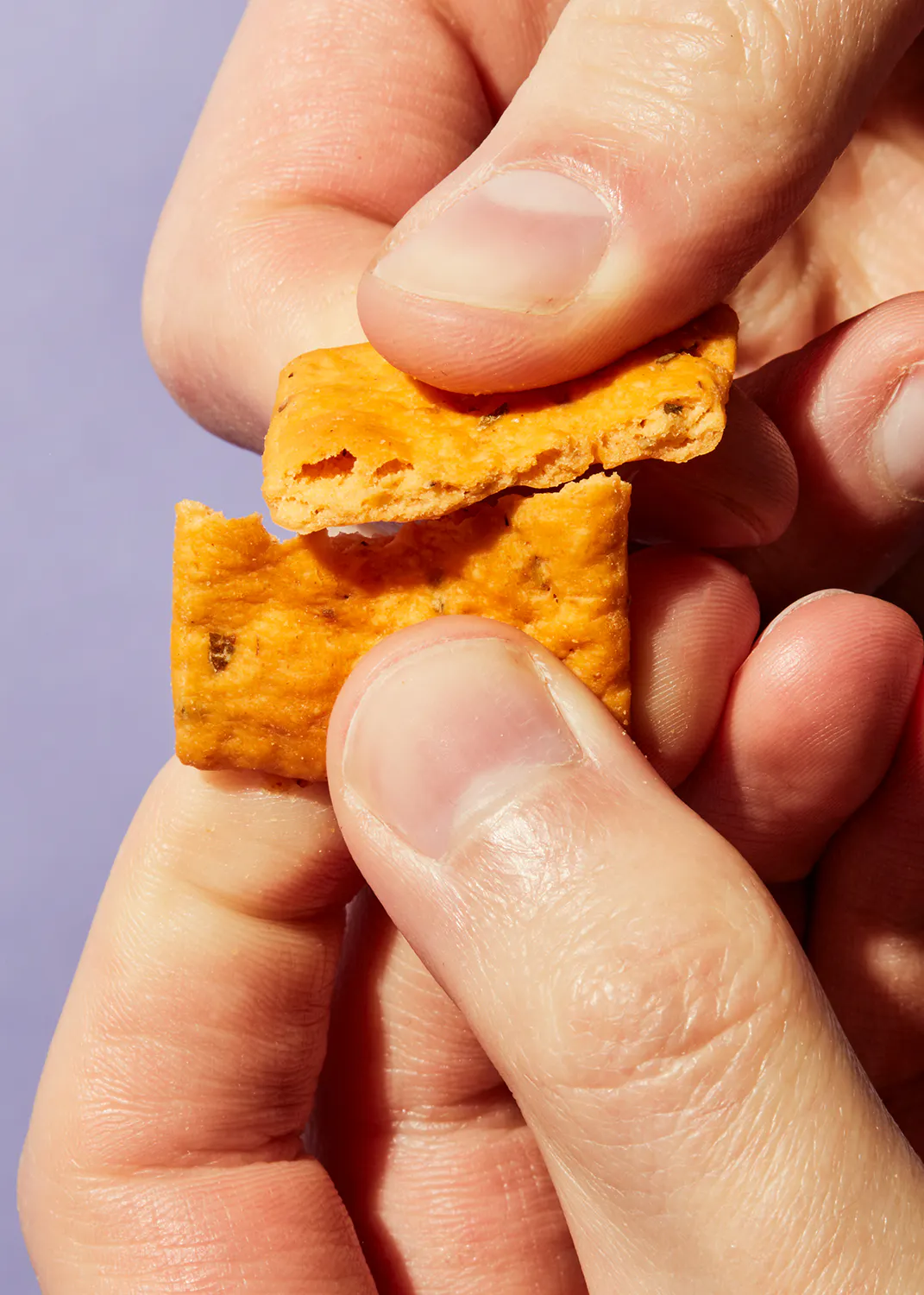 a close up of a person holding a cracker with a bite taken out of it