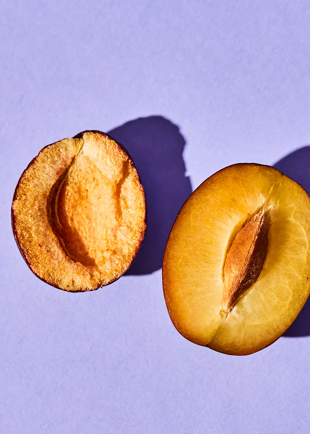 eine halbe Pflaume neben einer ganzen Pflaume auf einem lila Hintergrund