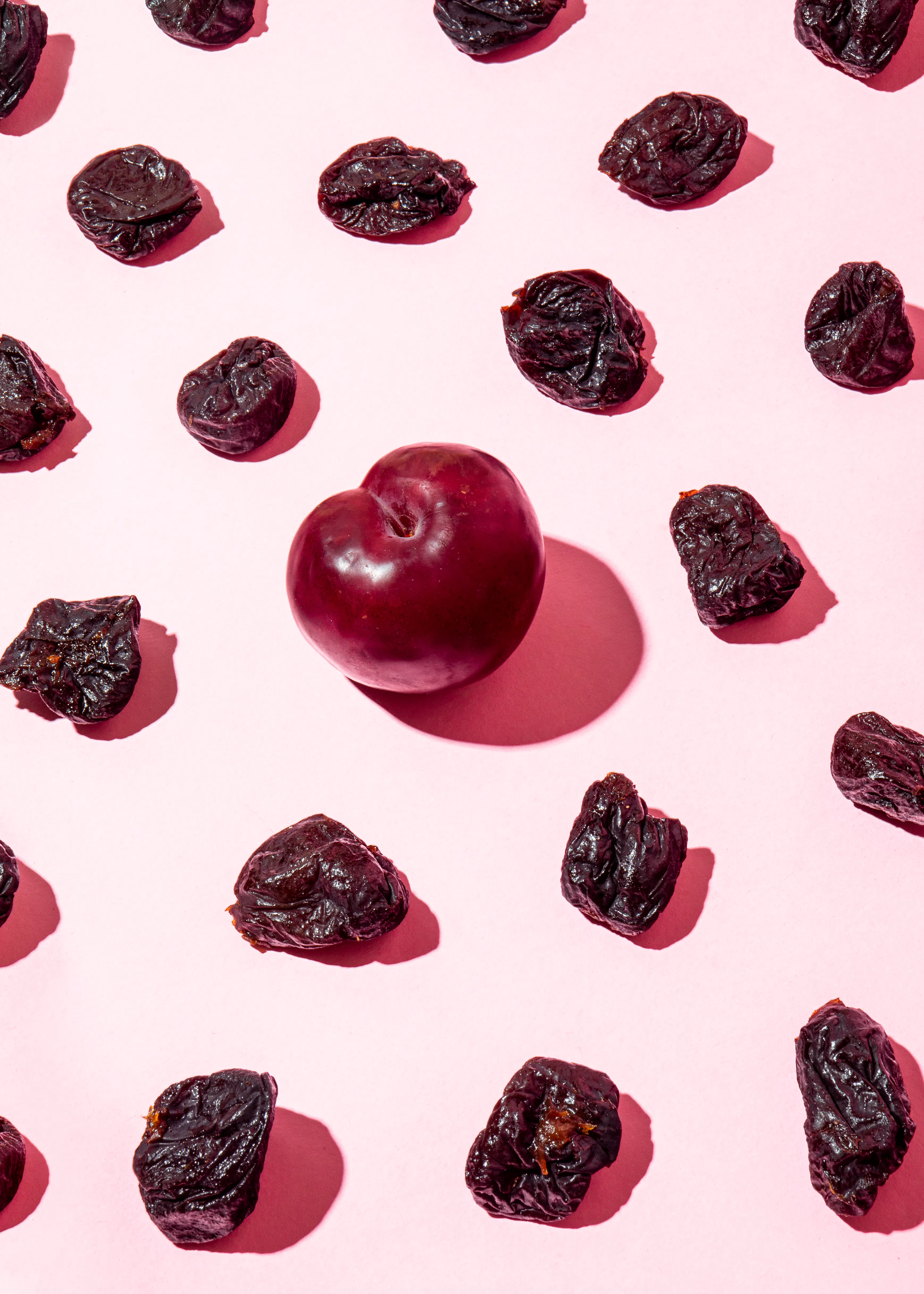eine Reihe von getrockneten Pflaumen auf rosa Hintergrund