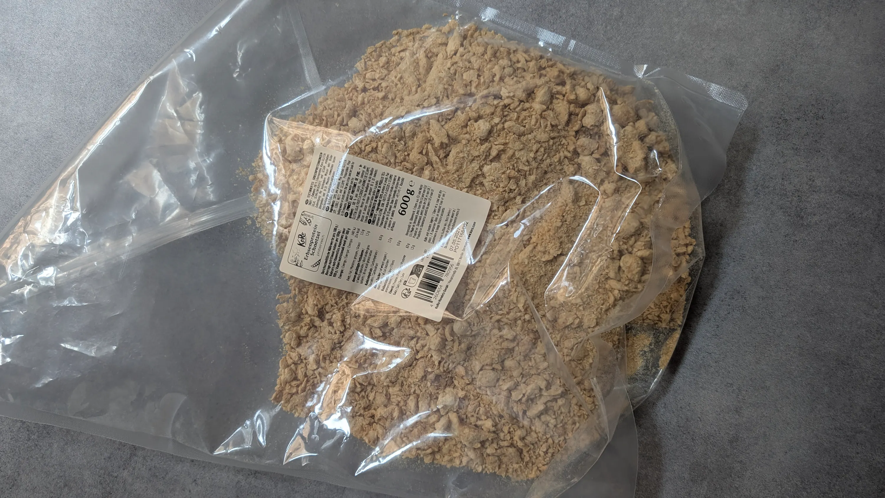 eine durchsichtige plastiktüte mit hellem, körnigem erbsenprotein auf einer dunklen oberfläche, mit einem etikett, das 600g anzeigt.