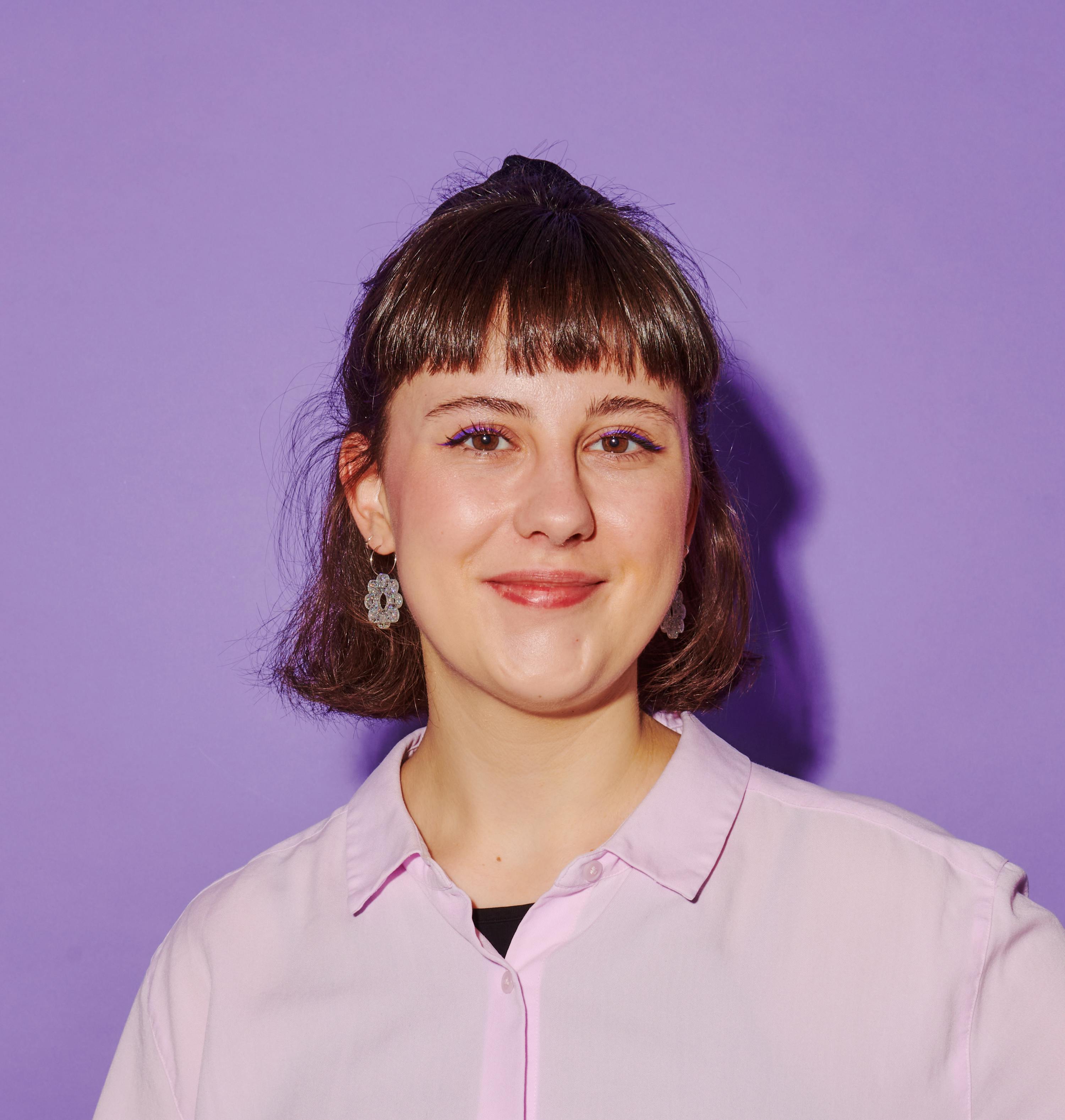 a woman wearing a pink shirt and earrings smiles for the camera