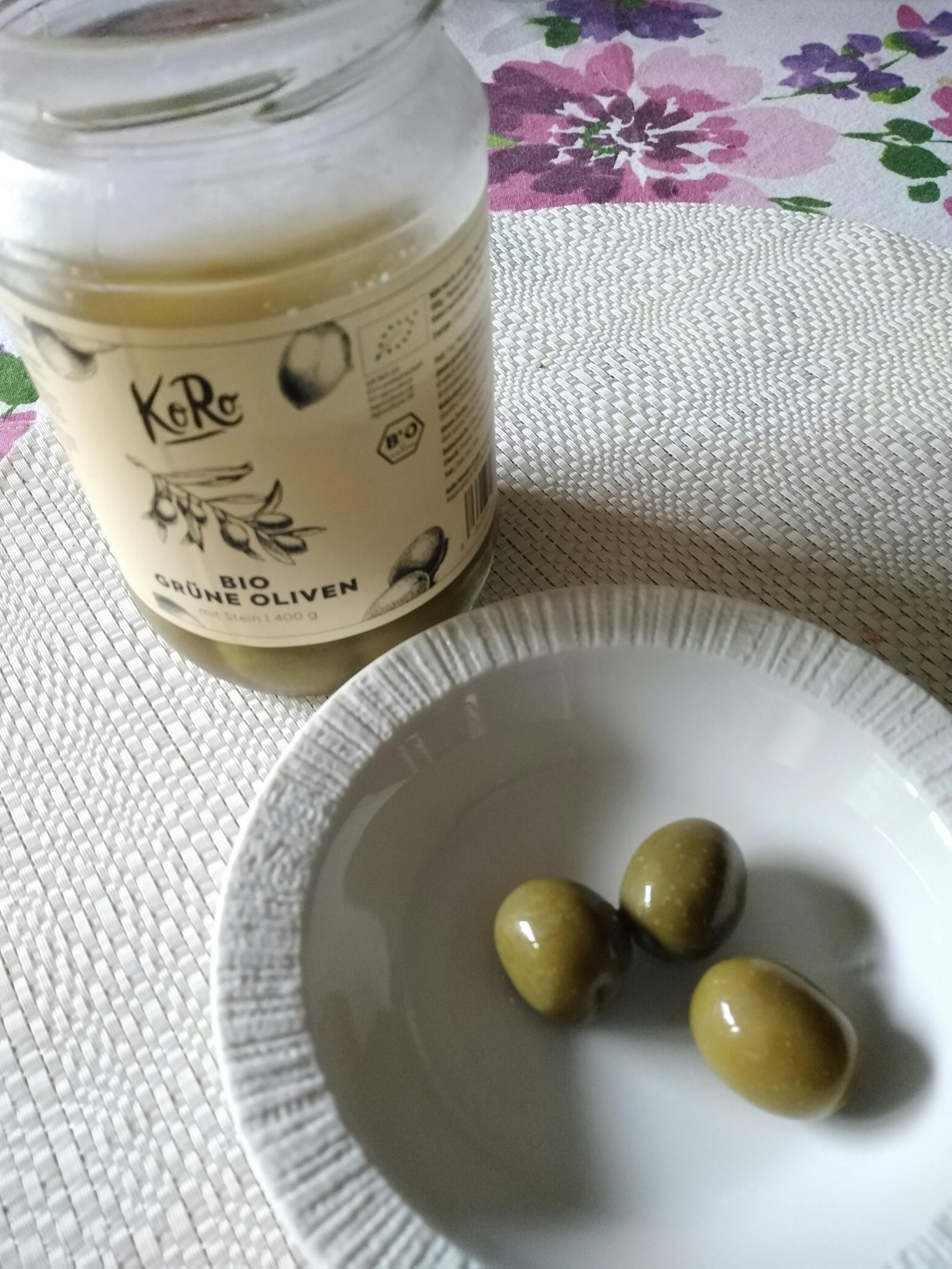 a jar of green olives next to a plate of green olives