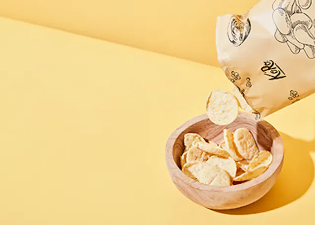 eine Tüte Kartoffelchips fällt in eine Holzschale .