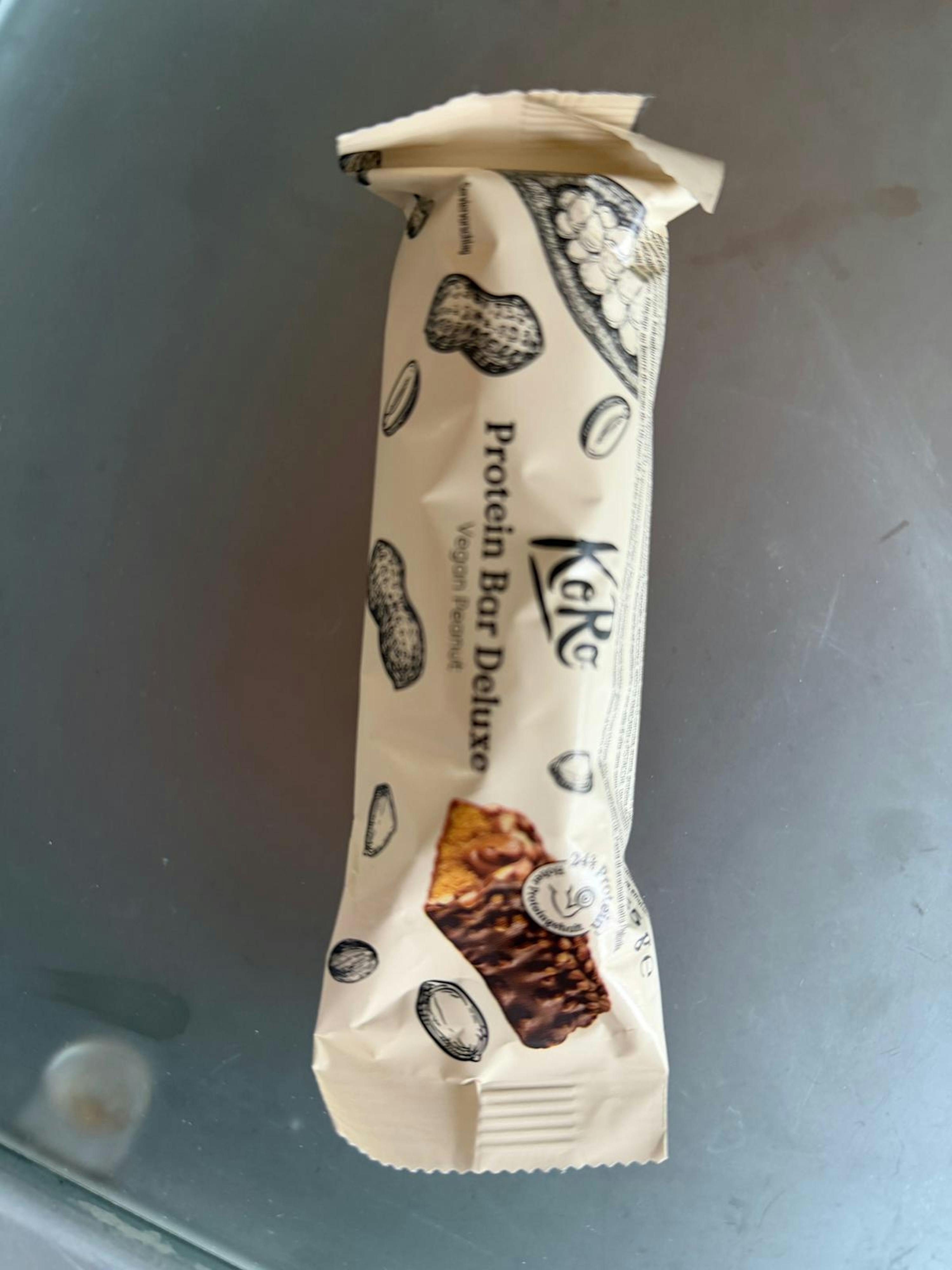 ein kore protein bar deluxe vegan peanut in einer hellen verpackung mit erdnussillustrationen und einem bild eines schokoladenüberzogenen riegels.